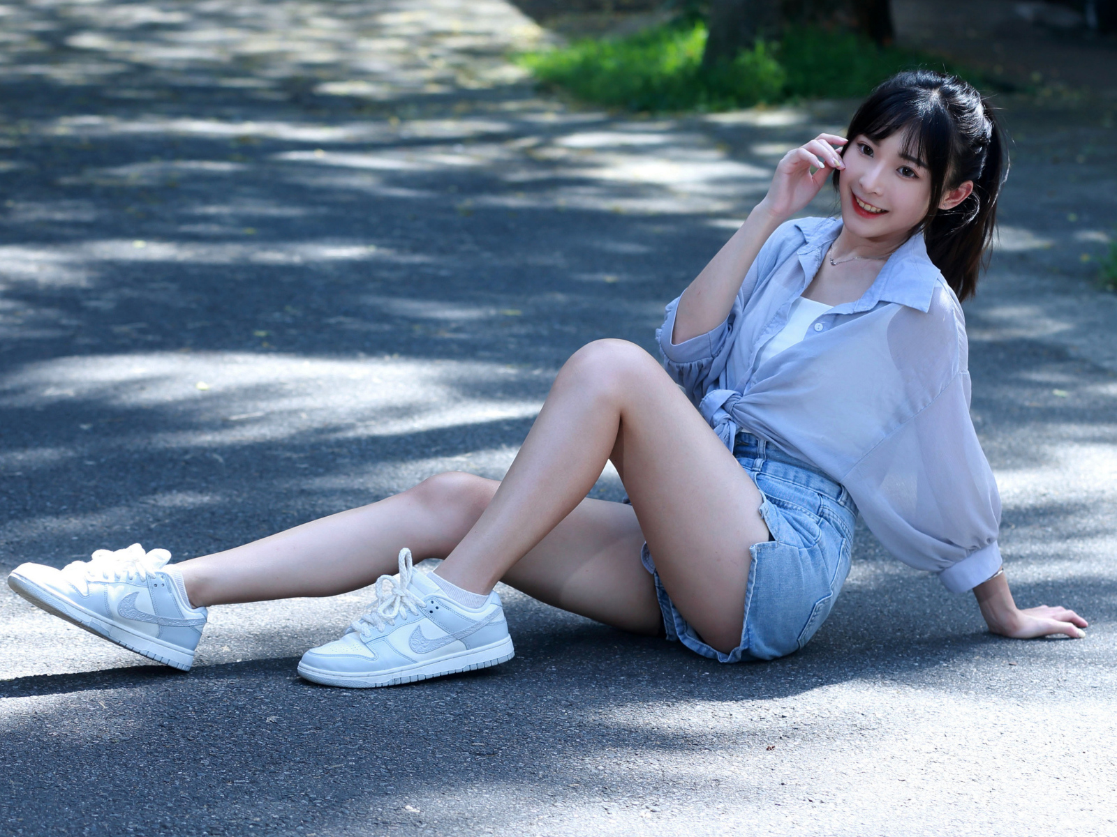 Улыбающаяся девушка азиатка в кедах сидит на дороге