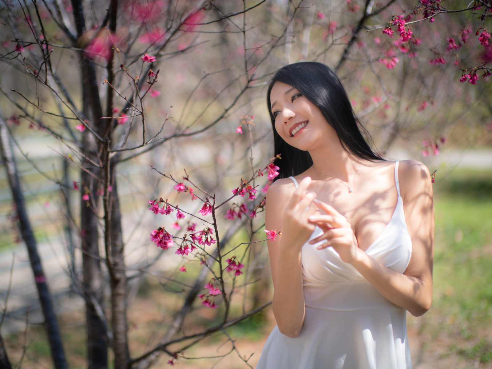 Улыбающаяся девушка в белом платье у дерева с цветами