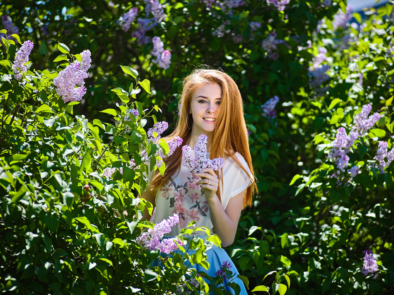 Улыбающаяся девушка стоит у куста сирени