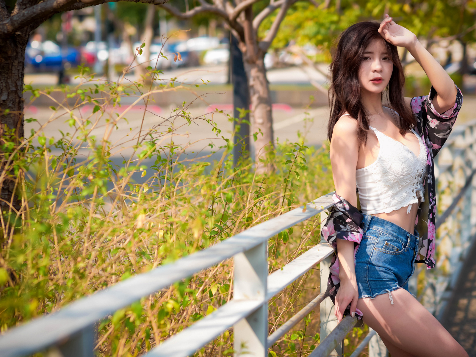 Молодая азиатка в синих шортах стоит у забора