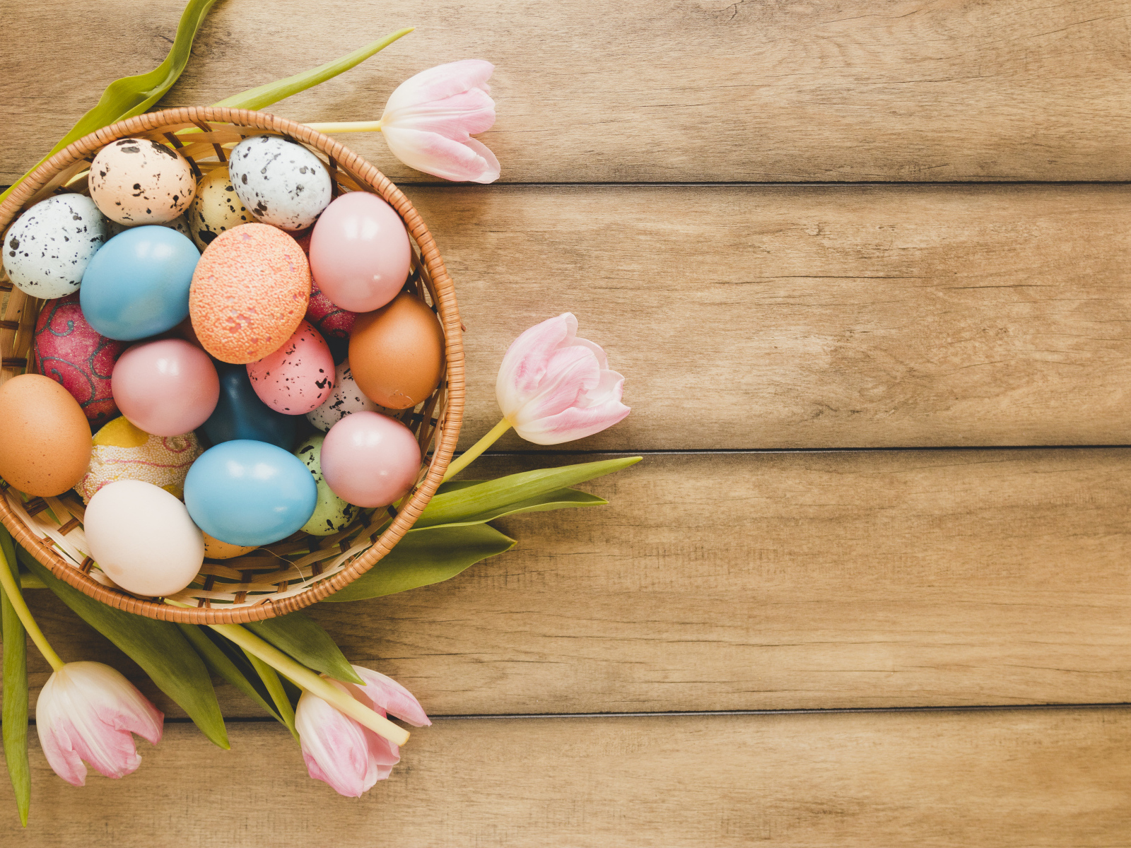 Корзина с крашеными яйцами и розовые тюльпаны на деревянном столе на Пасху