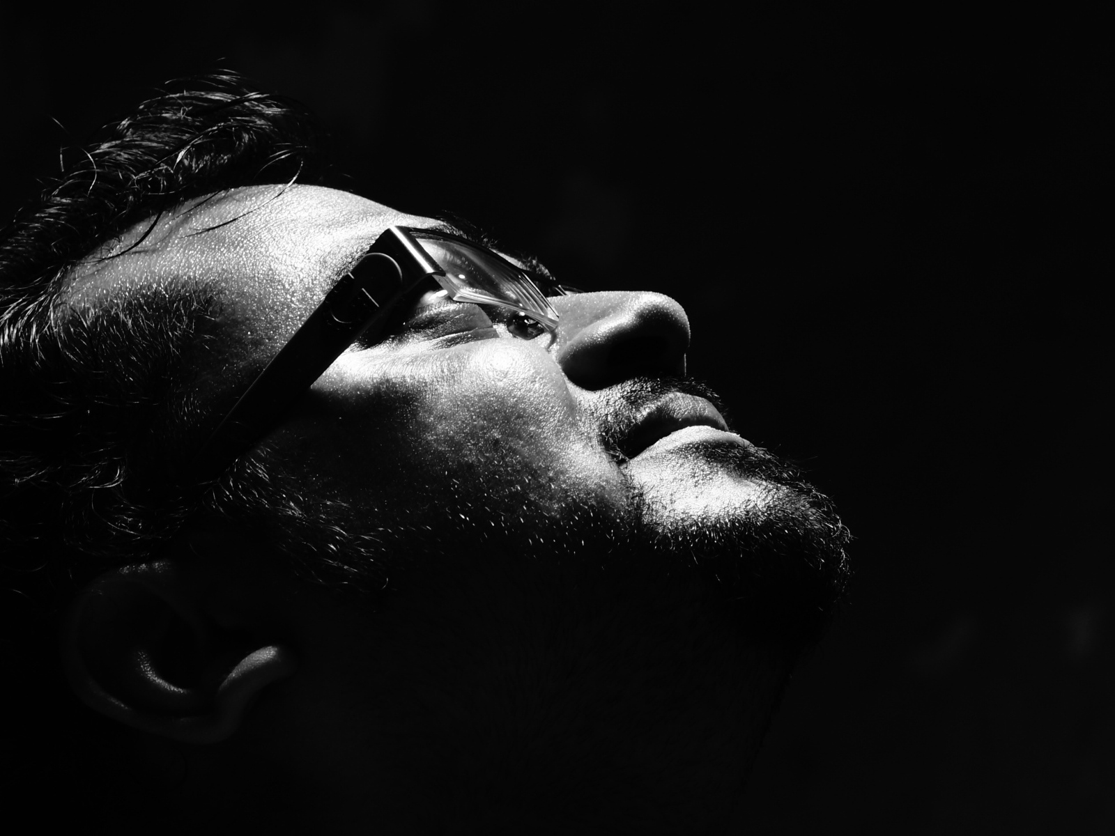 Мужчина в очках смотрит вверх на черном фоне