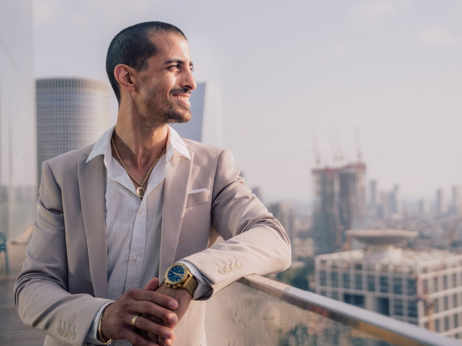 Улыбающийся стильный мужчина в костюме стоит на балконе 