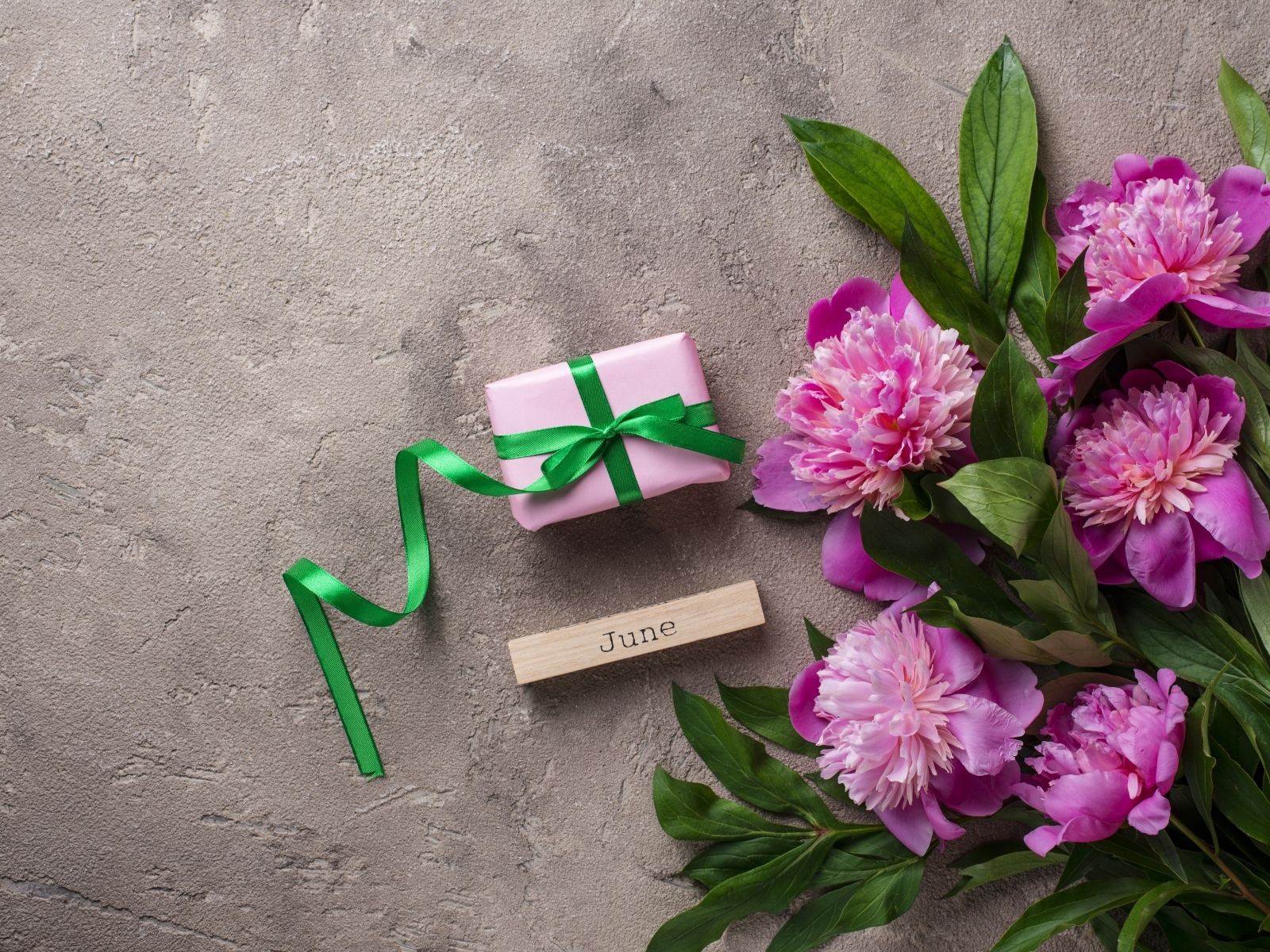 Букет розовых пионов с подарком на сером столе