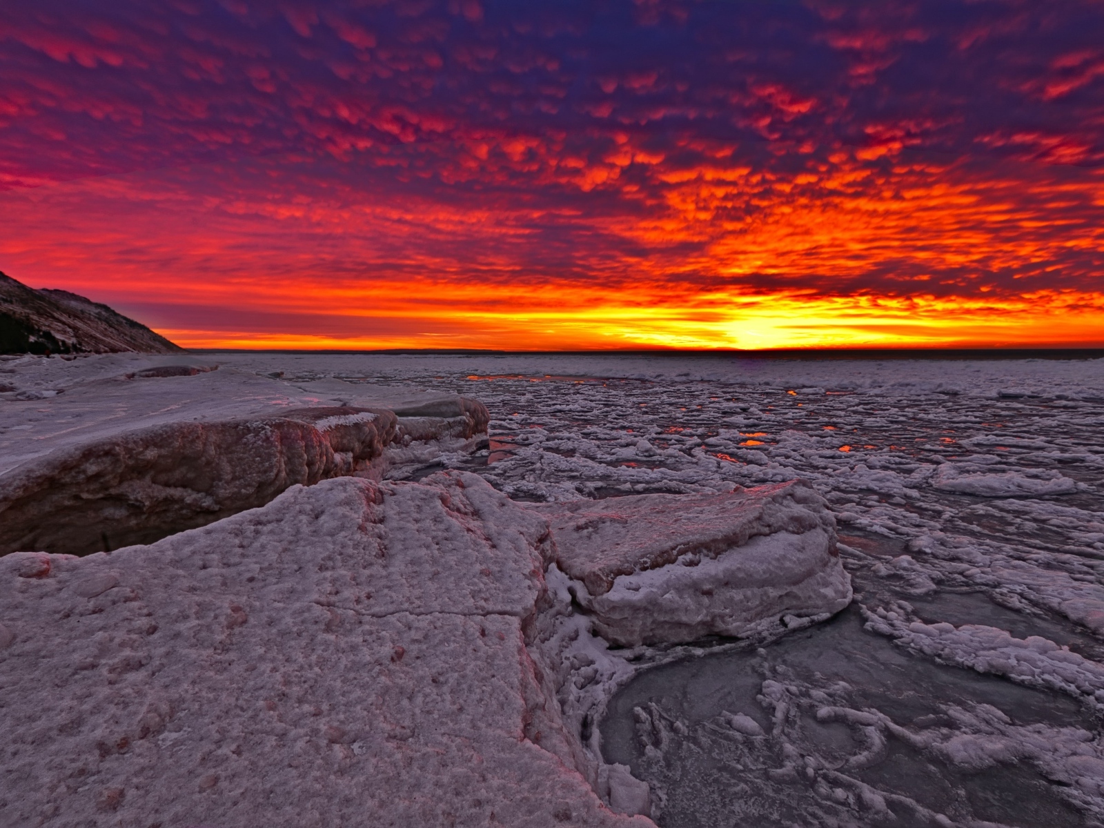 Красный закат солнца покрывает заледеневшее озеро 