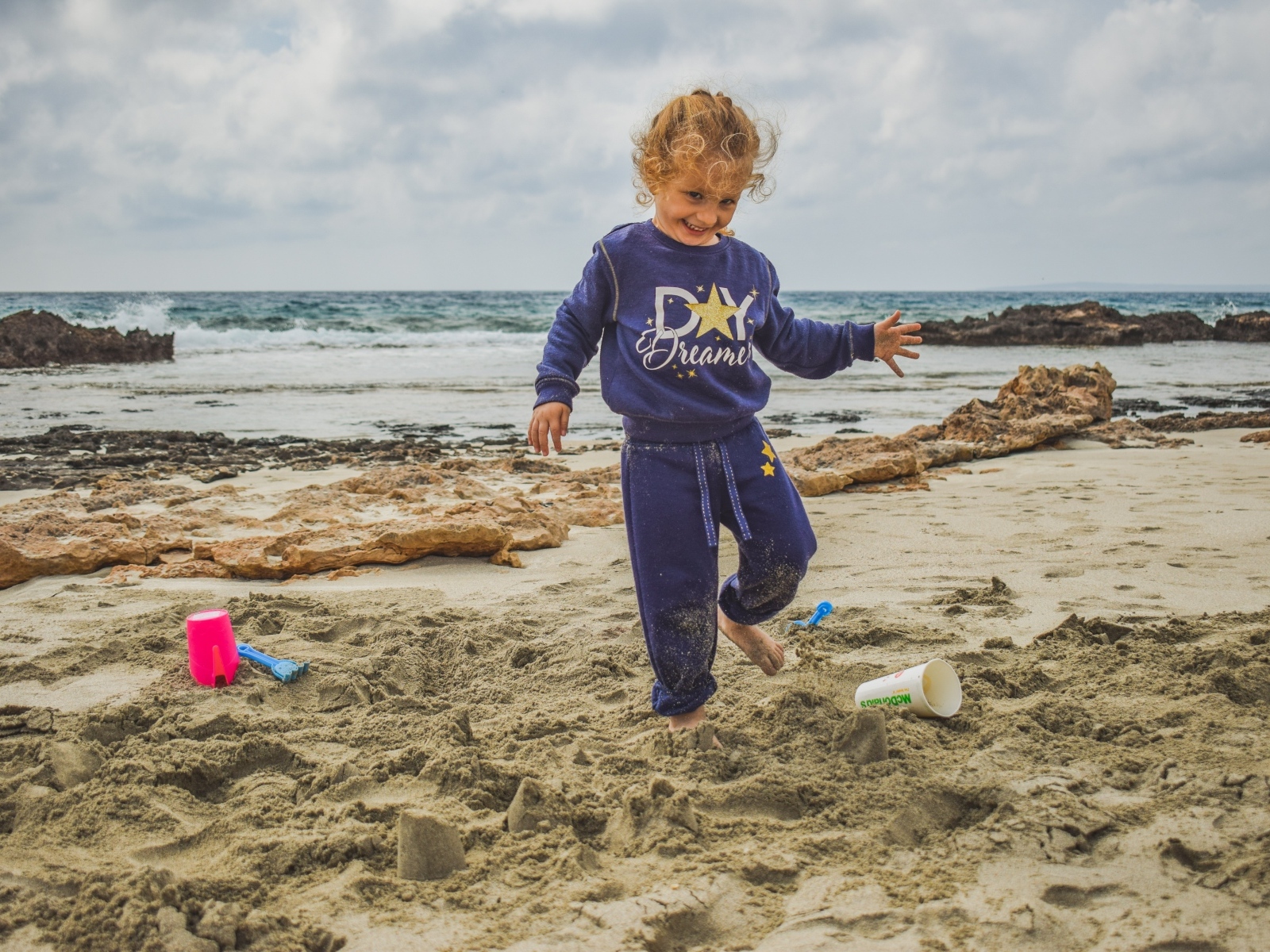 Веселая девочка играет на песке на пляже