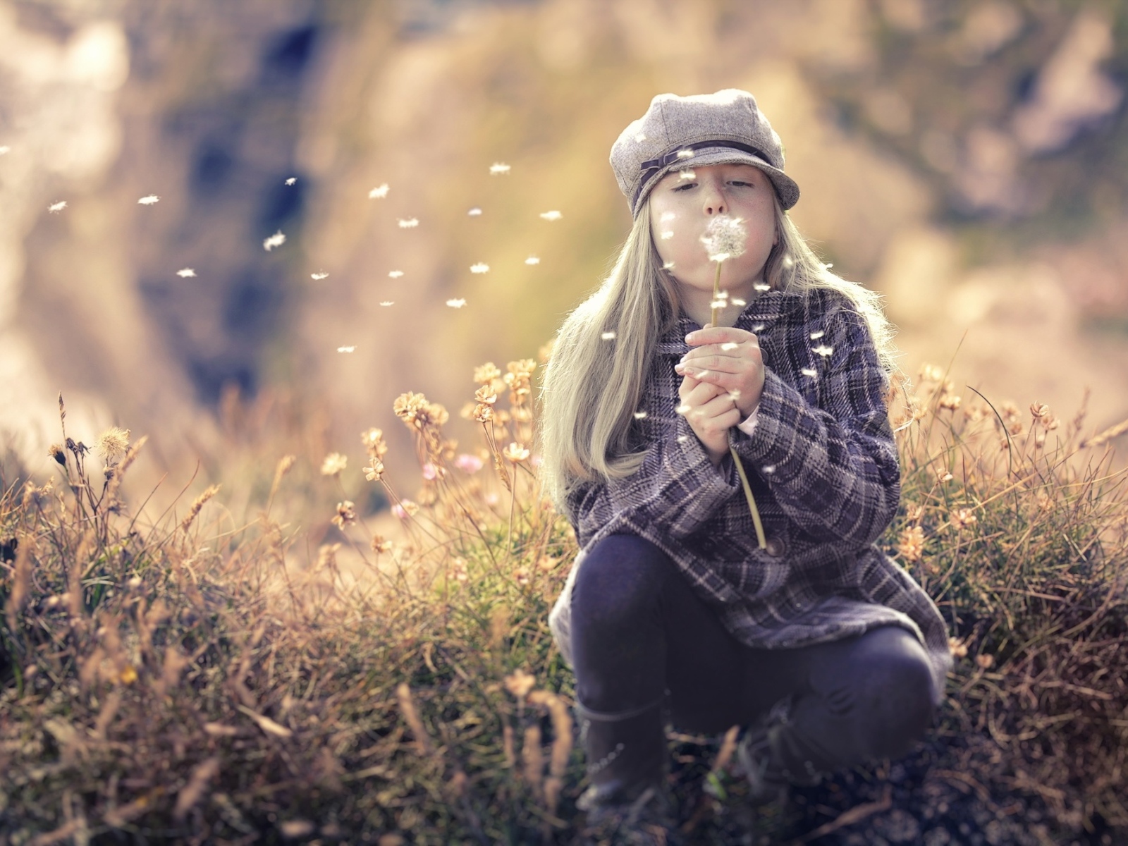 Девочка в кепке сдувает одуванчик
