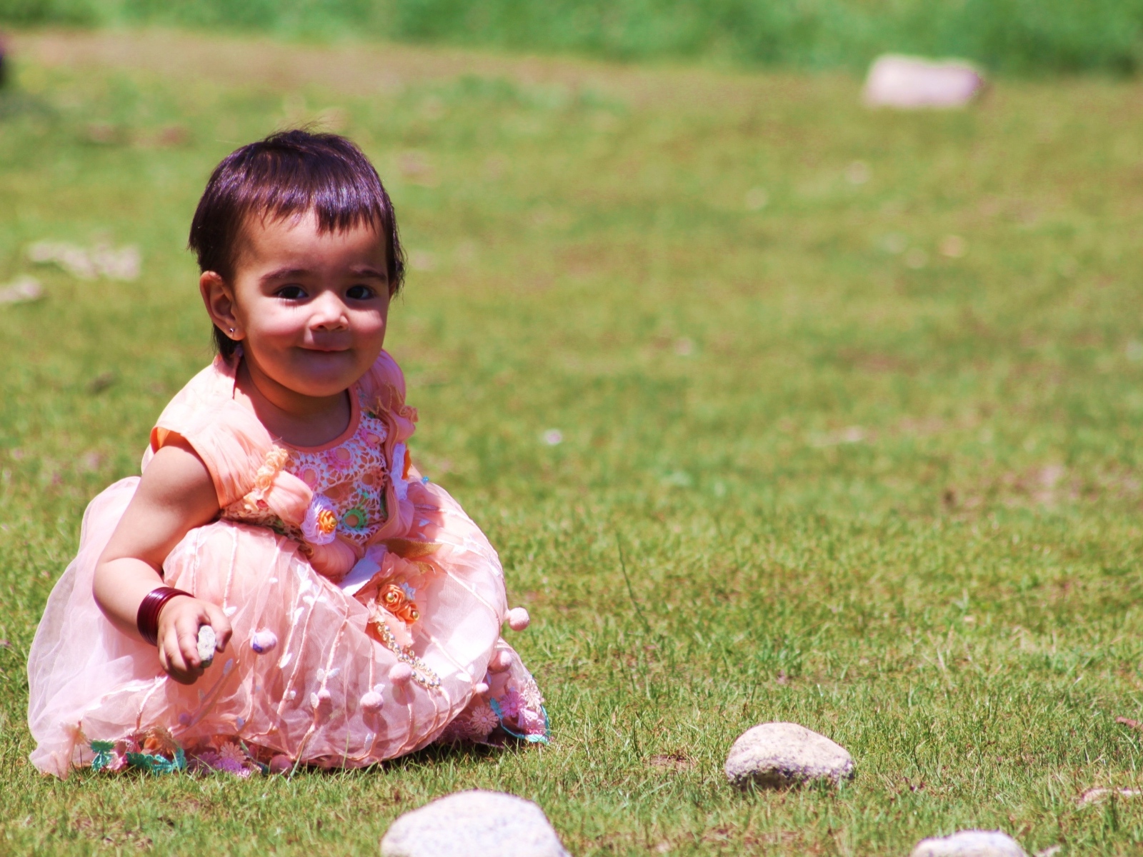 Девочка в розовом платье играет на зеленой траве