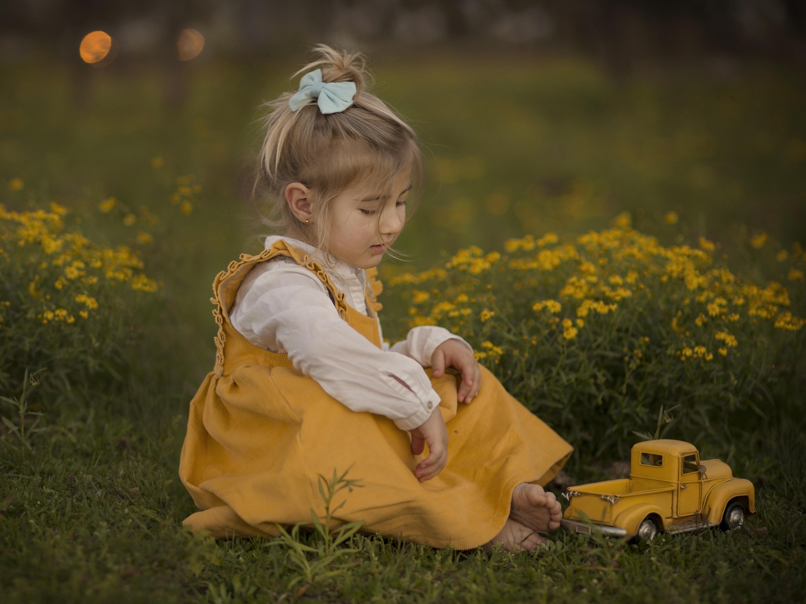 Девочка сидит на траве с игрушечной машинкой