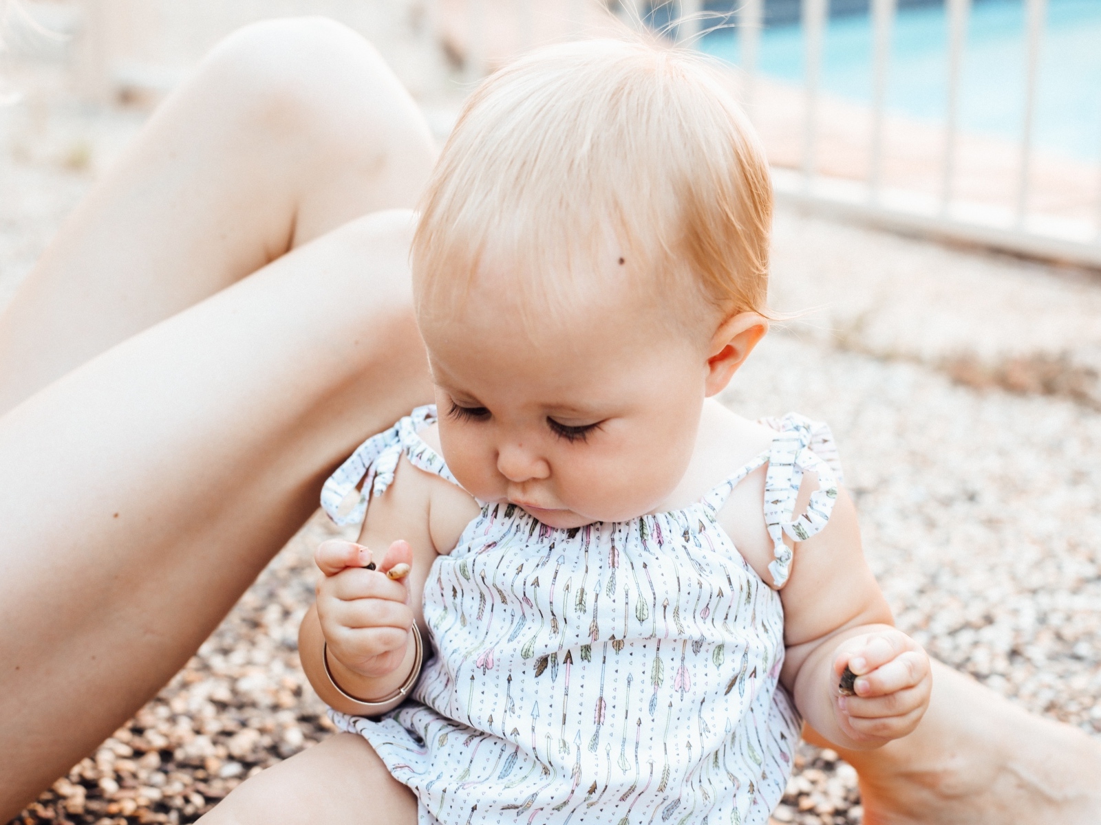 Маленькая светловолосая девочка сидит на песке