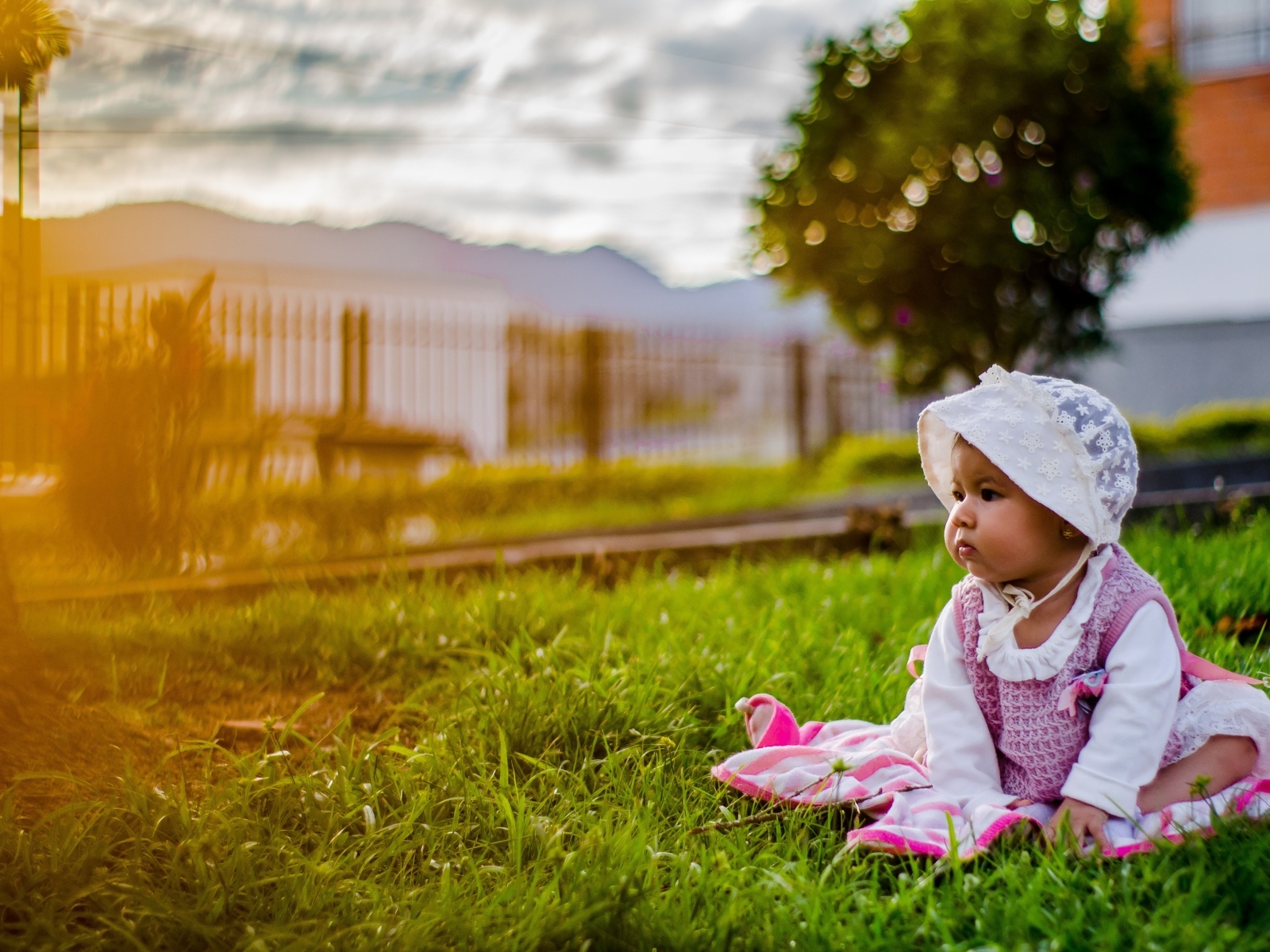 Маленькая девочка в розовом платье сидит на траве
