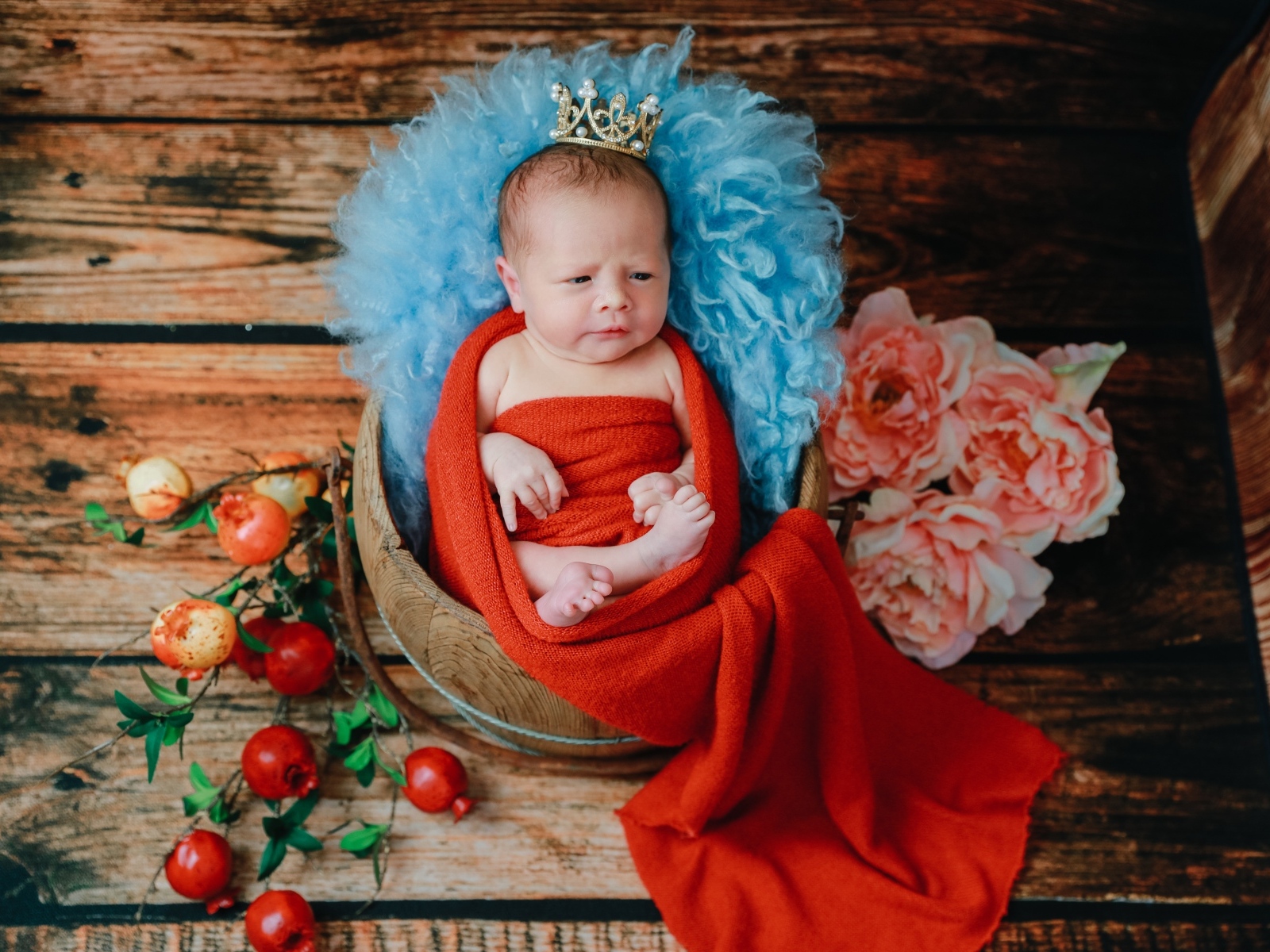 Новорожденный ребенок в красном покрывале с короной на голове 