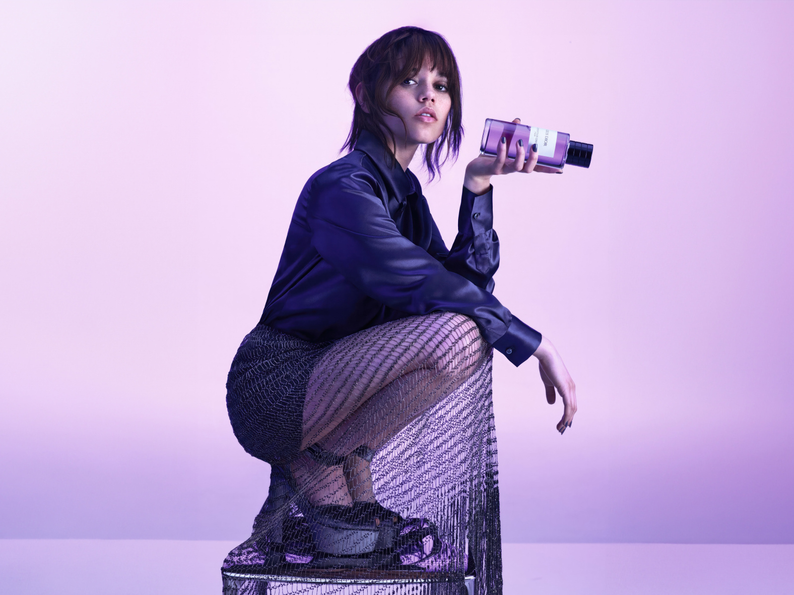 Актриса Дженна Ортега на стуле с духами в руках