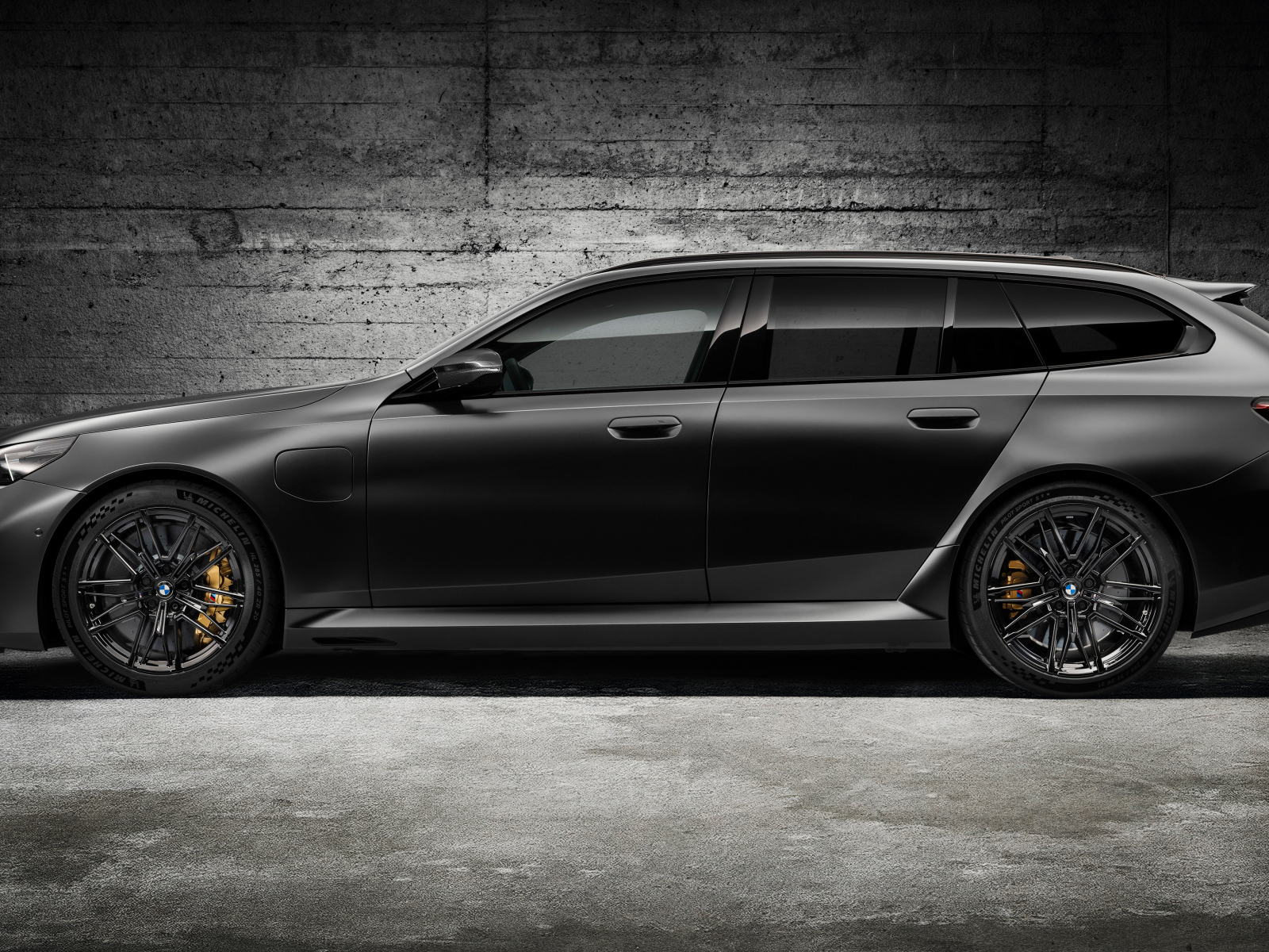 Вид сбоку на черный автомобиль BMW M5 Touring 2024 года