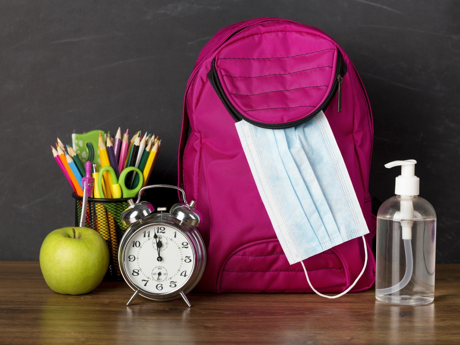 Рюкзак на столе с будильником, ручками и яблоком