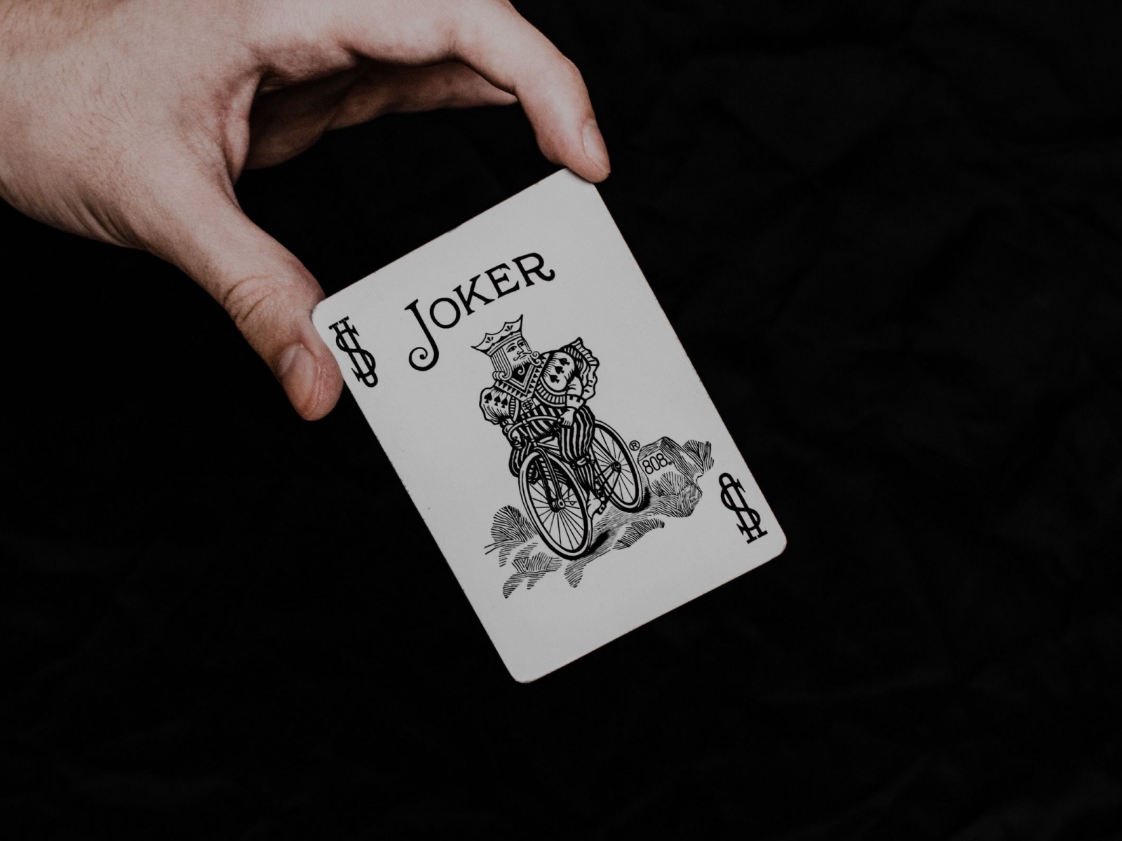 Карта Джокер в руке на черном фоне