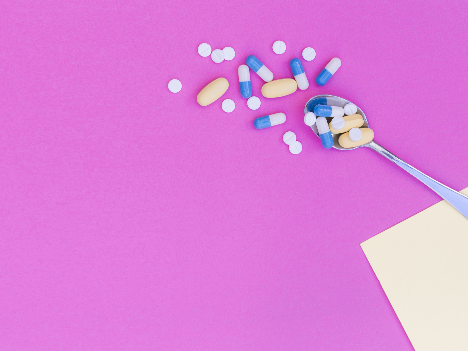 Таблетки с ложкой на розовом фоне