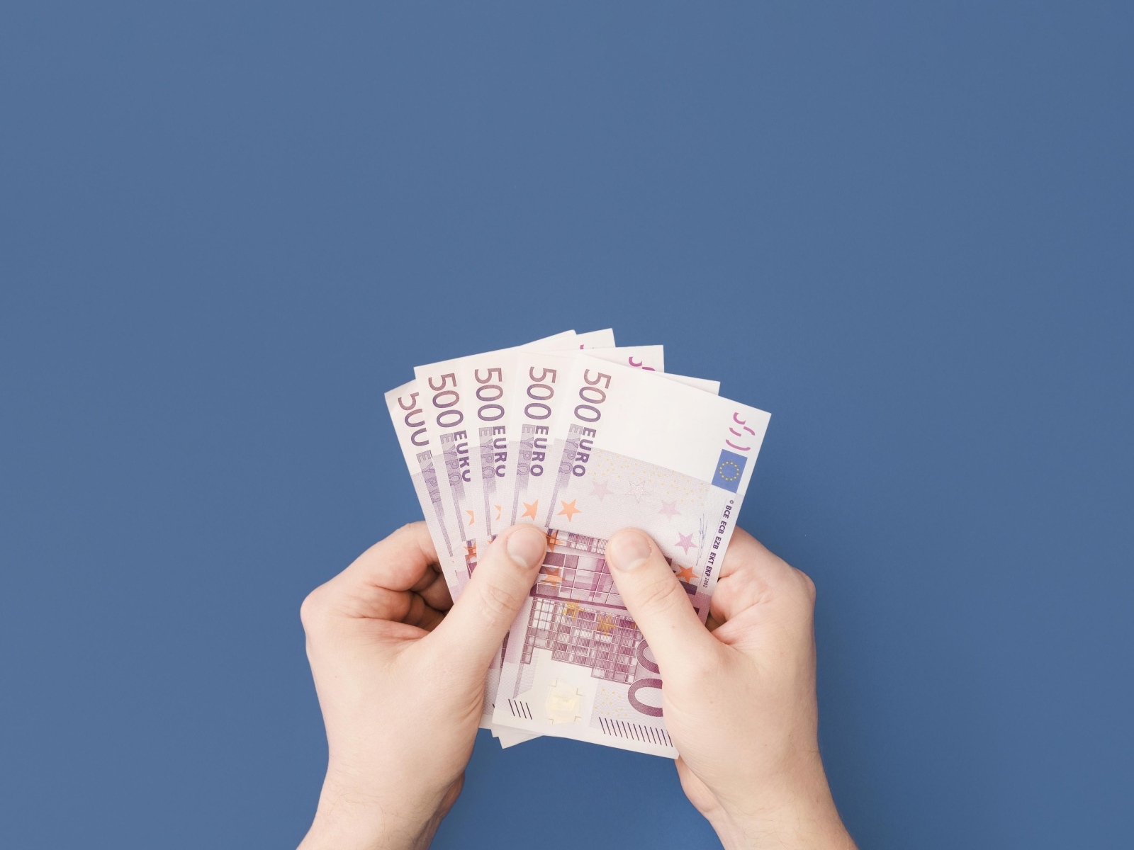 Купюры в пятьсот евро в руках на синем фоне