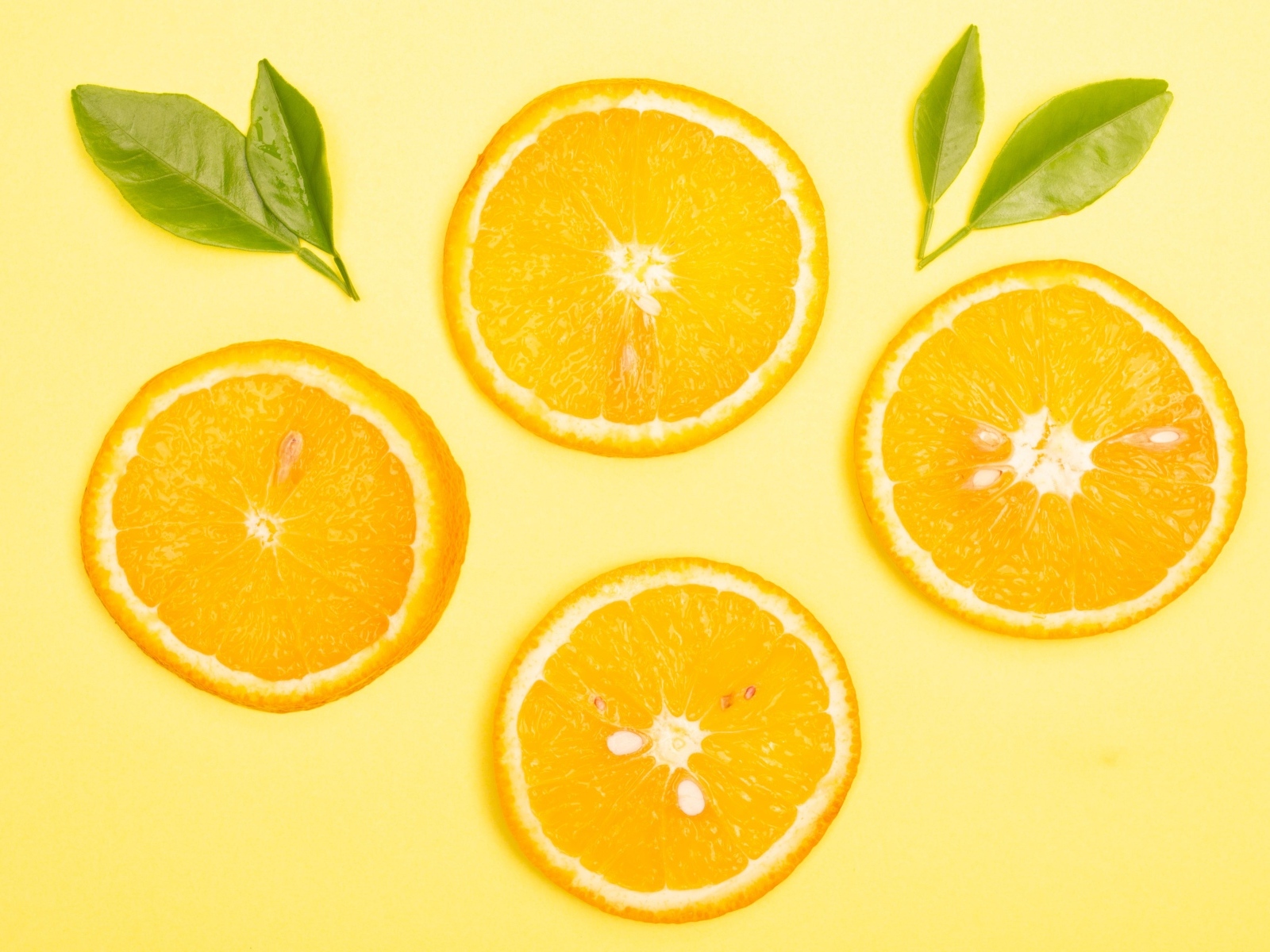Нарезанный апельсин с зелеными листьями на желтом фоне