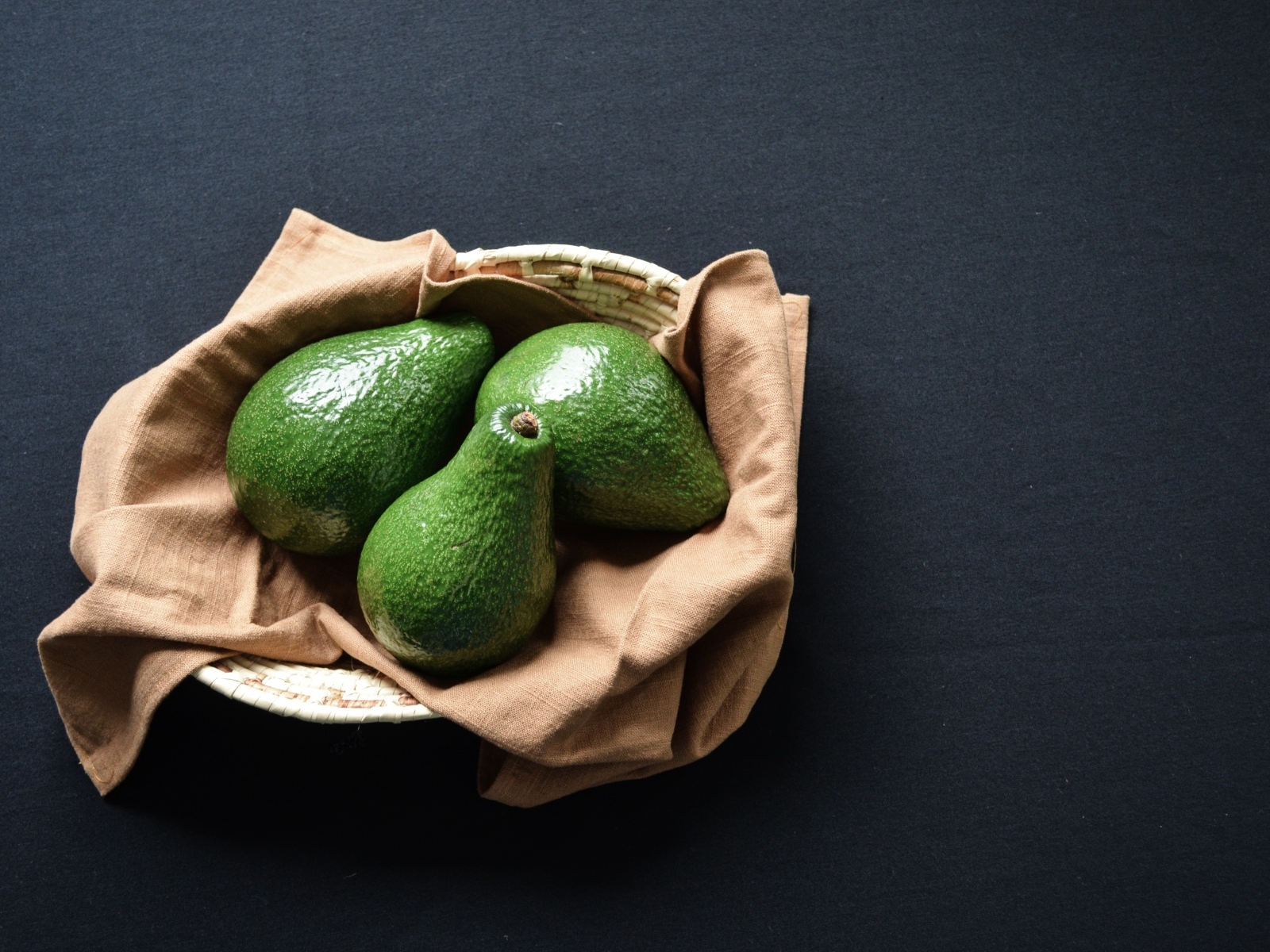Три зеленых авокадо в корзинке на столе