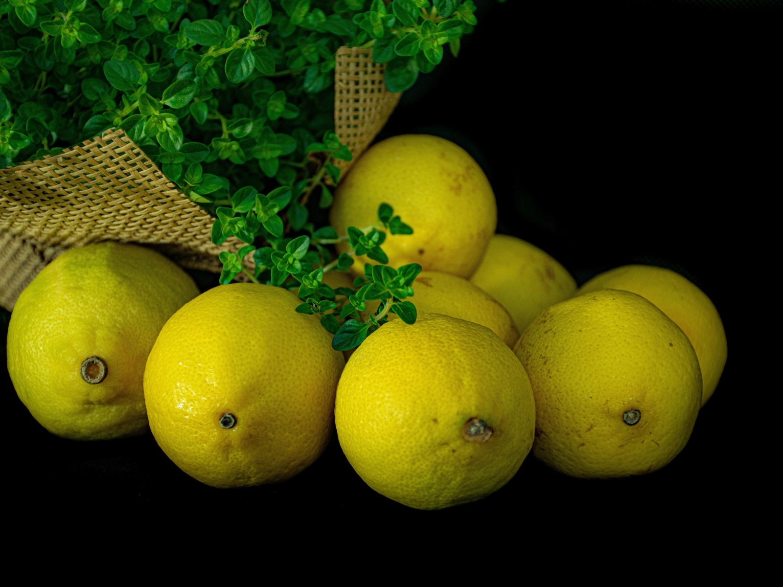 Желтые лимоны на черном столе с зеленью