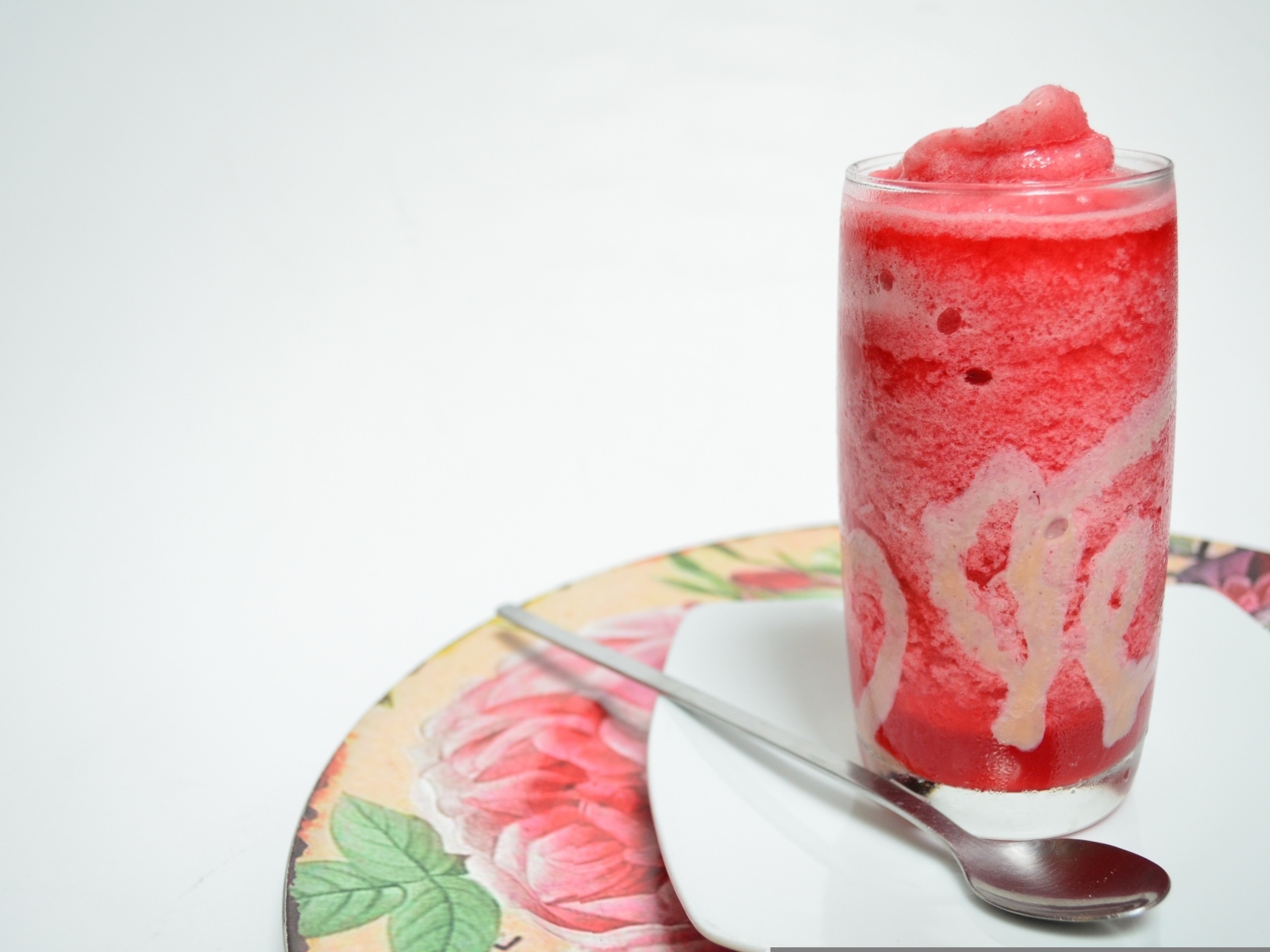 Стакан красного ягодного смузи на столе с чайной ложкой