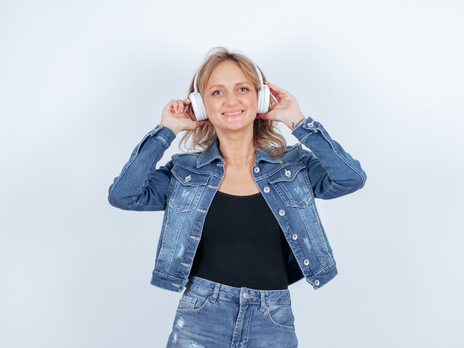 Девушка в джинсовом костюме с наушниками на голове на фоне стены