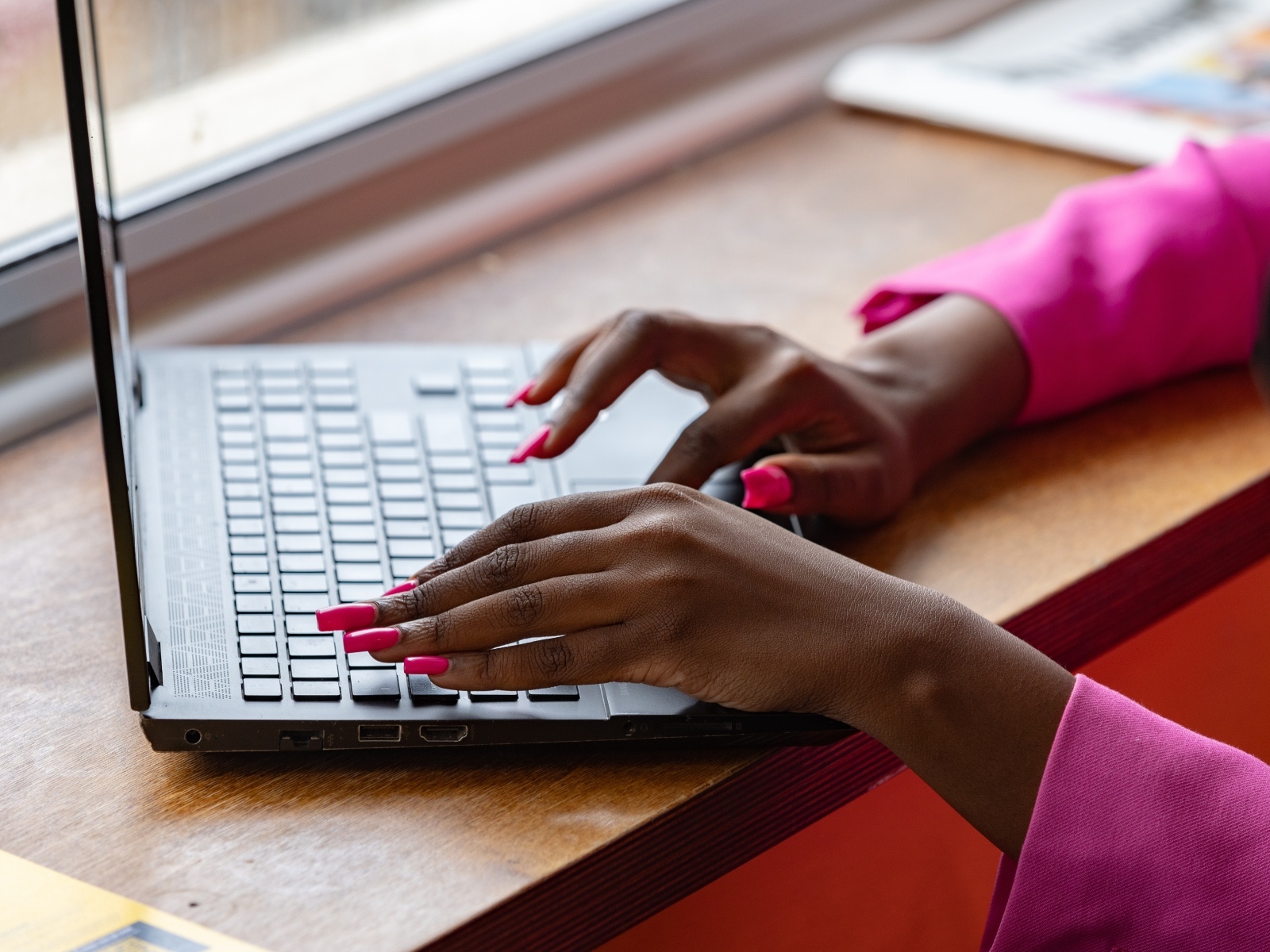 Девушка с розовым маникюром сидит за ноутбуком