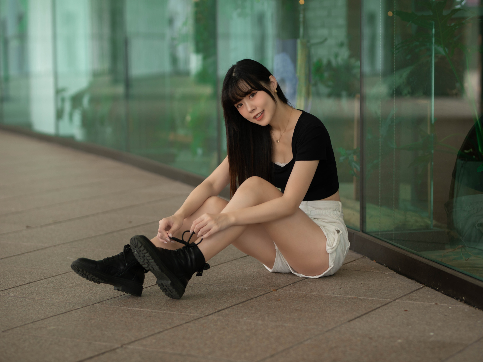 Азиатка в шортах сидит у стеклянной стены