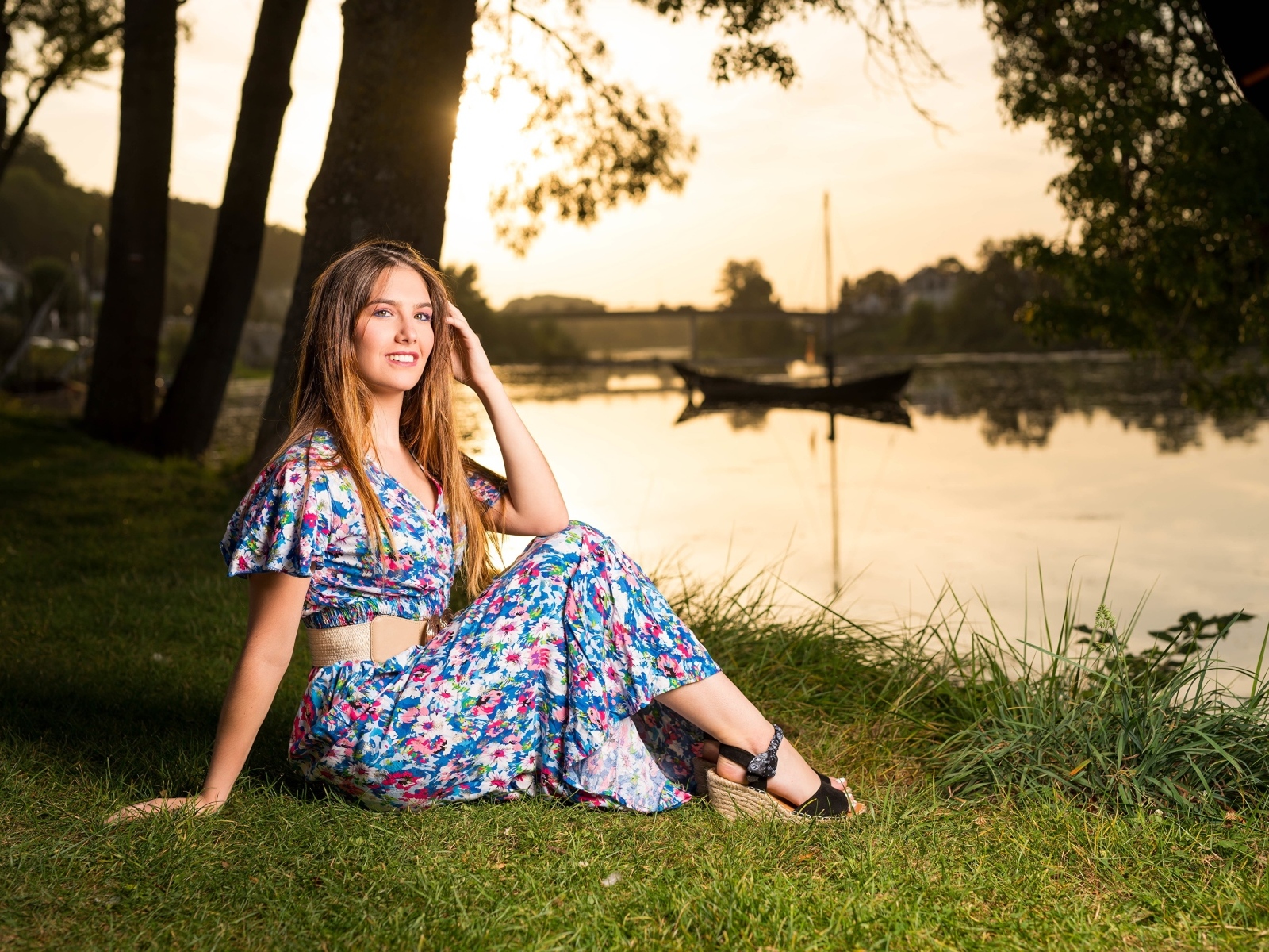 Милая девушка в платье сидит на берегу реки в парке