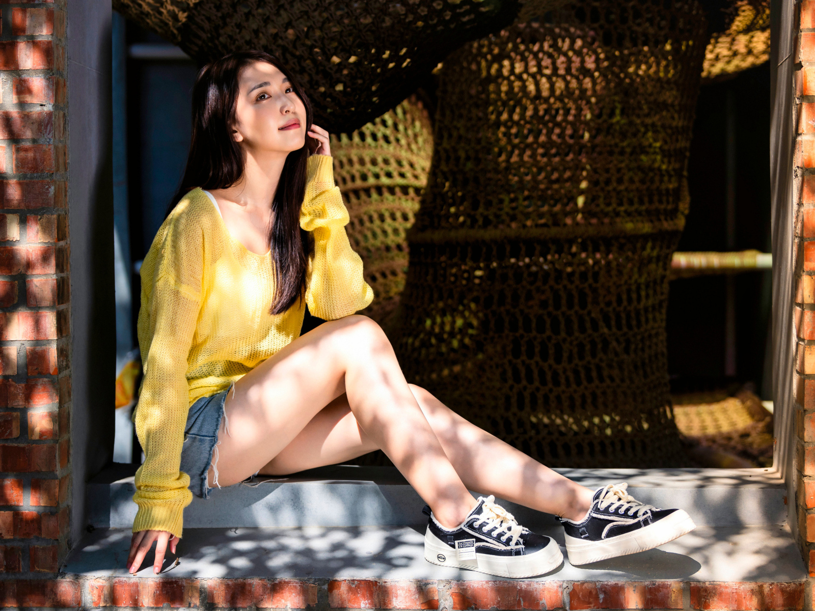 Мечтательная молодая девушка азиатка сидит на окне