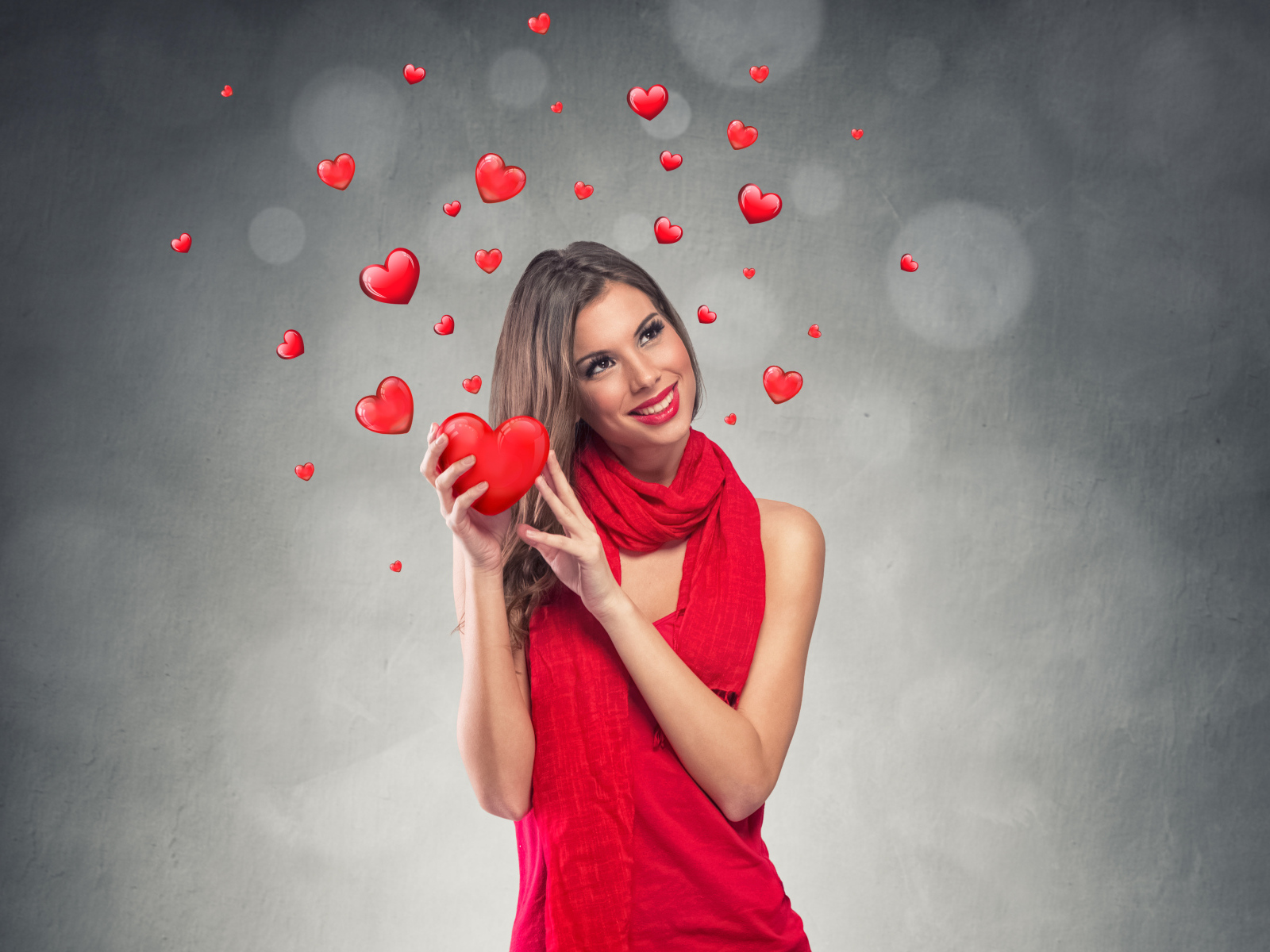 Улыбающаяся девушка в красном платье с сердечками на сером фоне