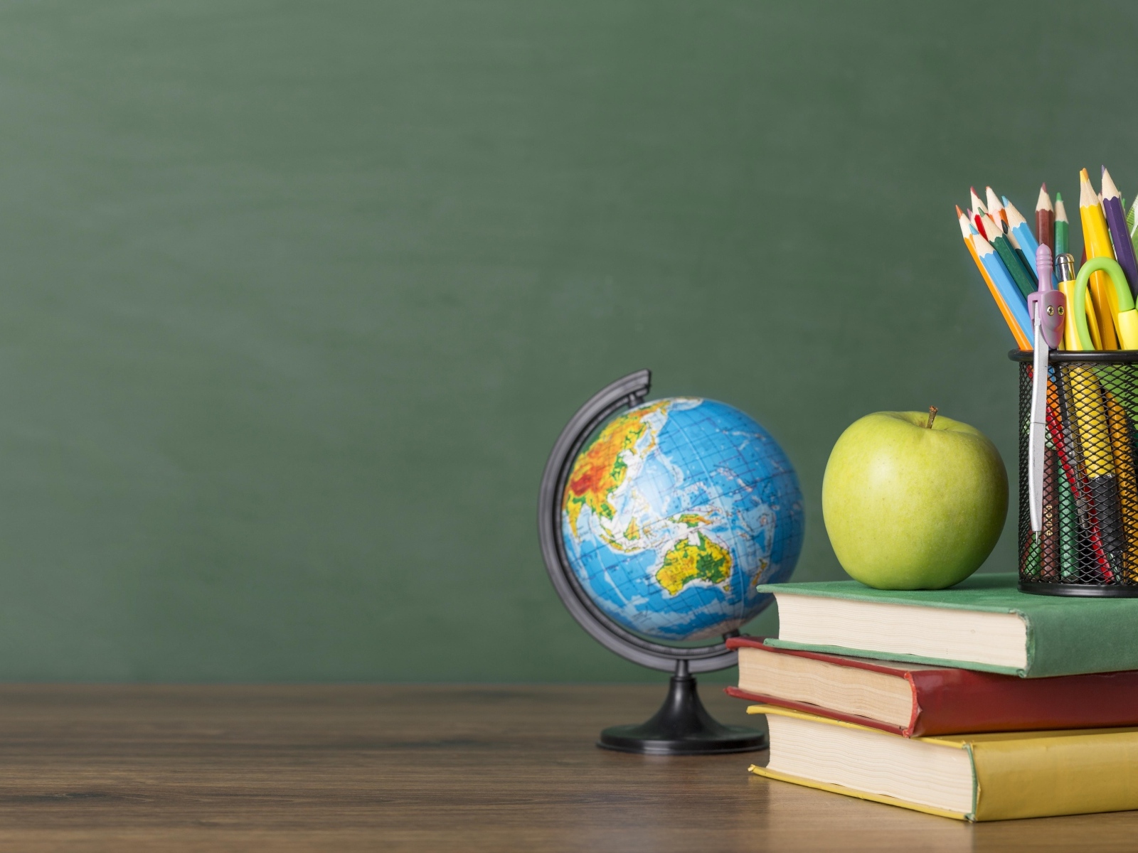 Книги на столе с глобусом, яблоком и ручками в школе