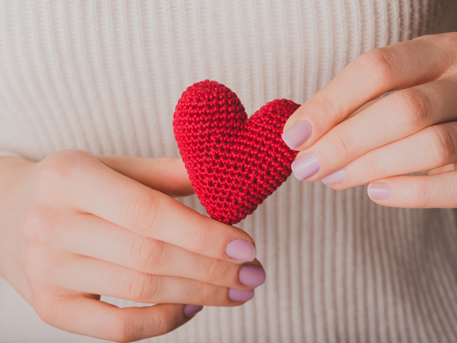 Девушка держит в руке вязаное красное сердце