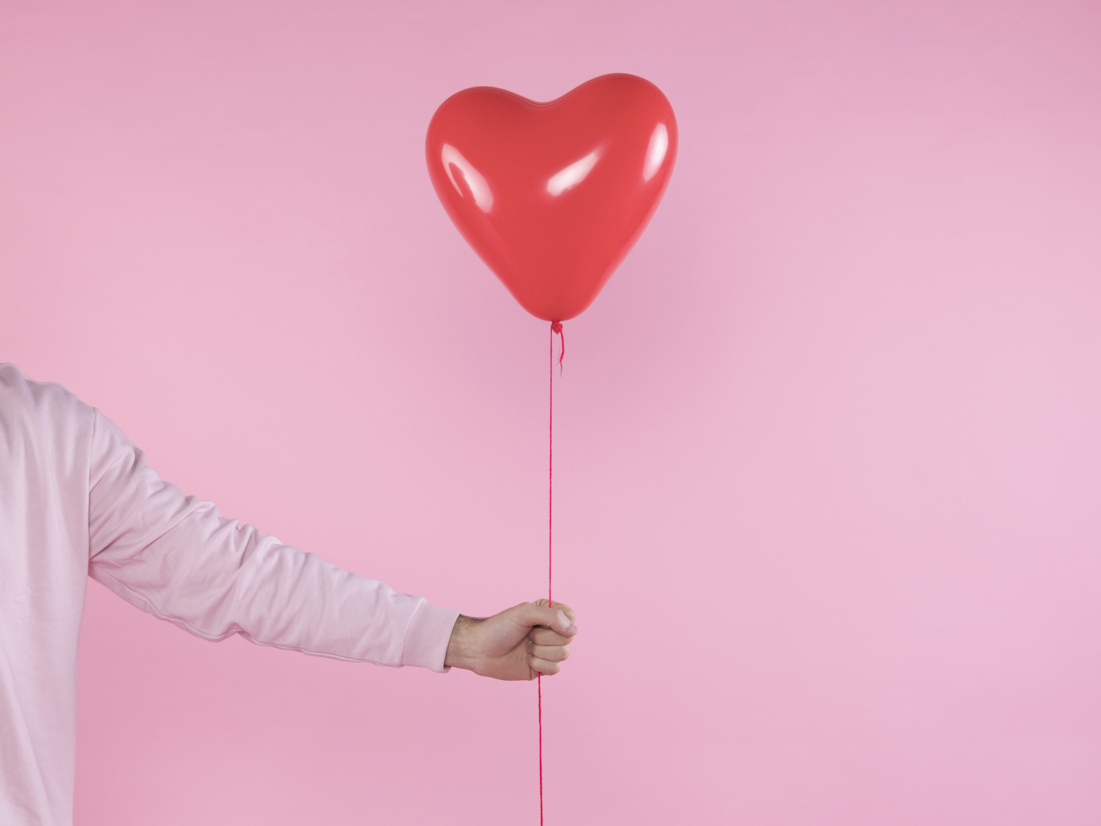 Шарик в форме сердца в руке на розовом фоне