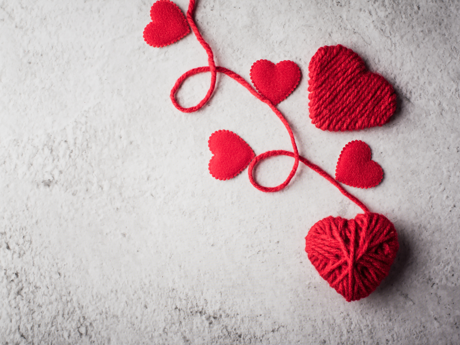 Сердечки из красной шерстяной нити на сером фоне