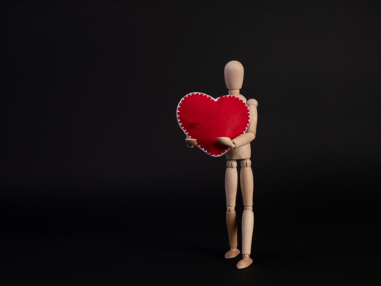 Марионетка держит красное сердце на черном фоне