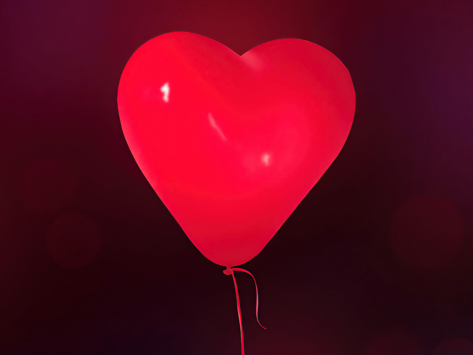 Красный шарик в форме сердца на фоне стены