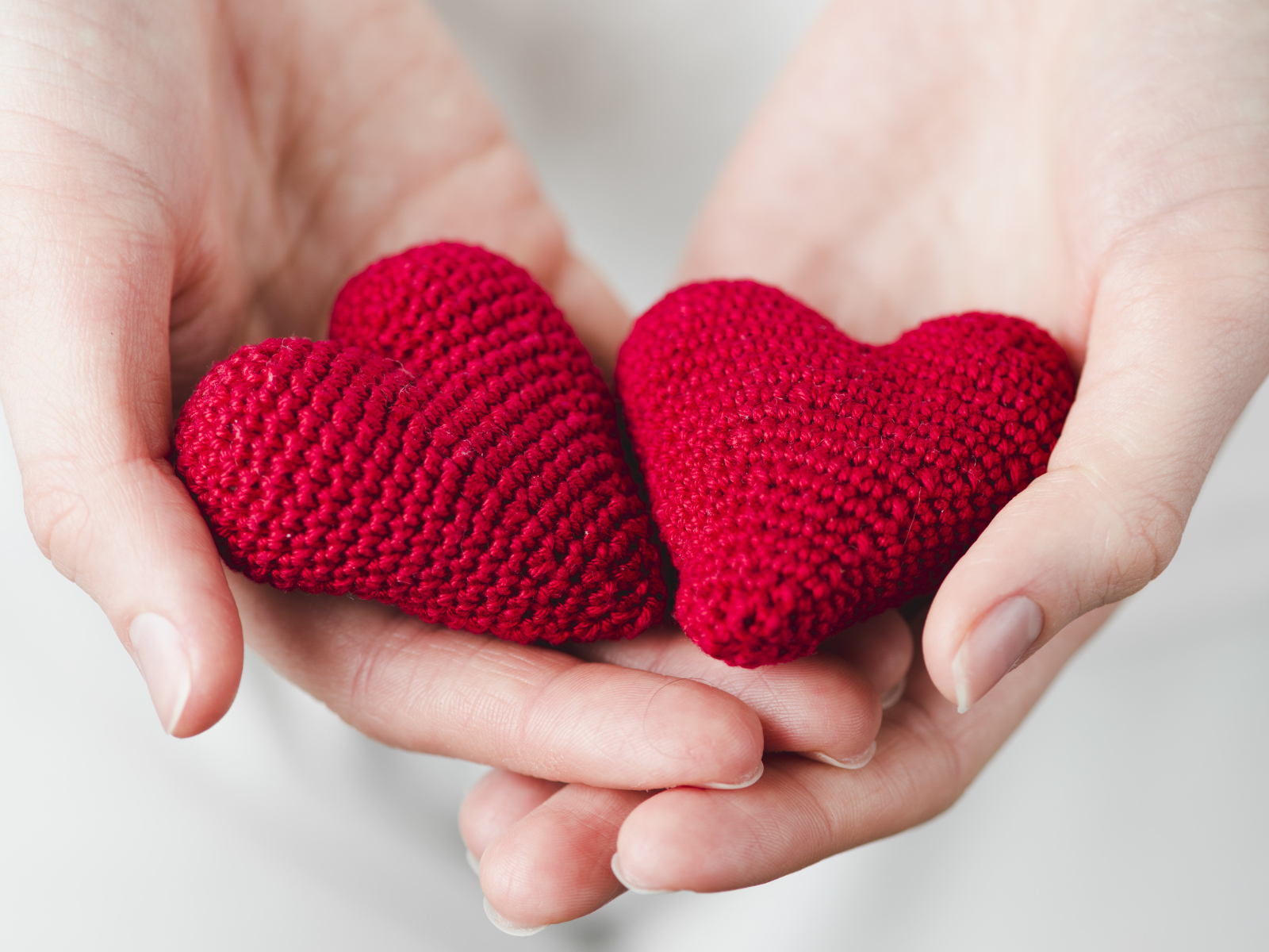 Два красных вязаных сердечка в руках девушки