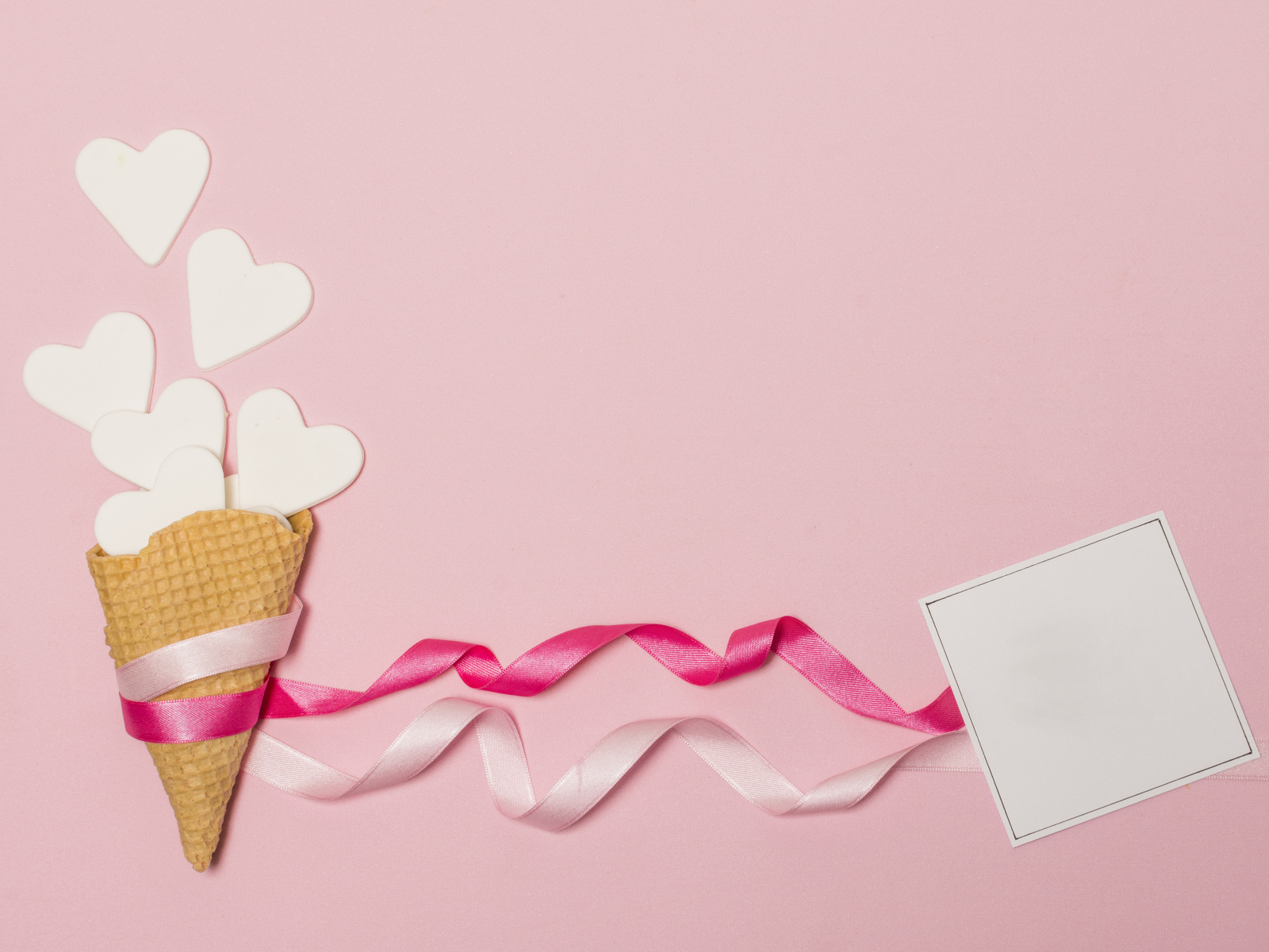 Вафельный рожок с сердечками, лентами и листом бумаги на розовом фоне