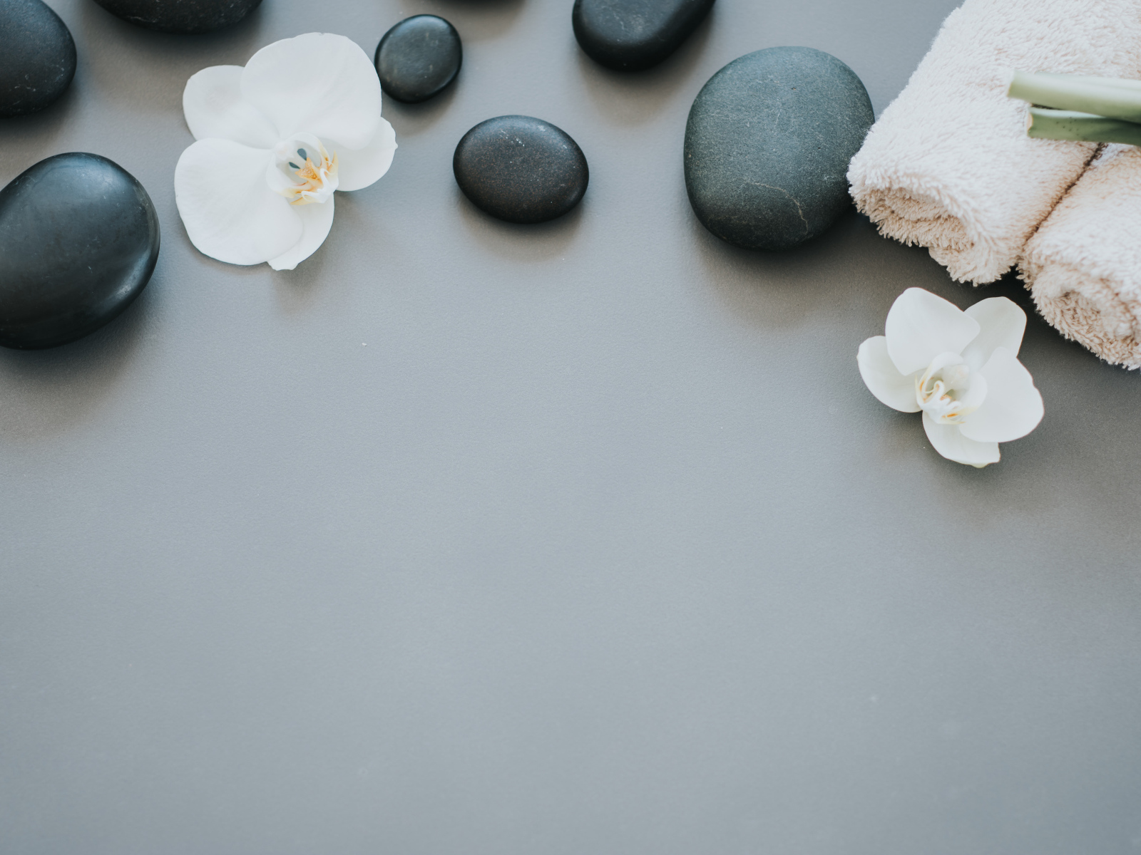 Черные камни с цветами орхидеи и полотенцем на сером фоне