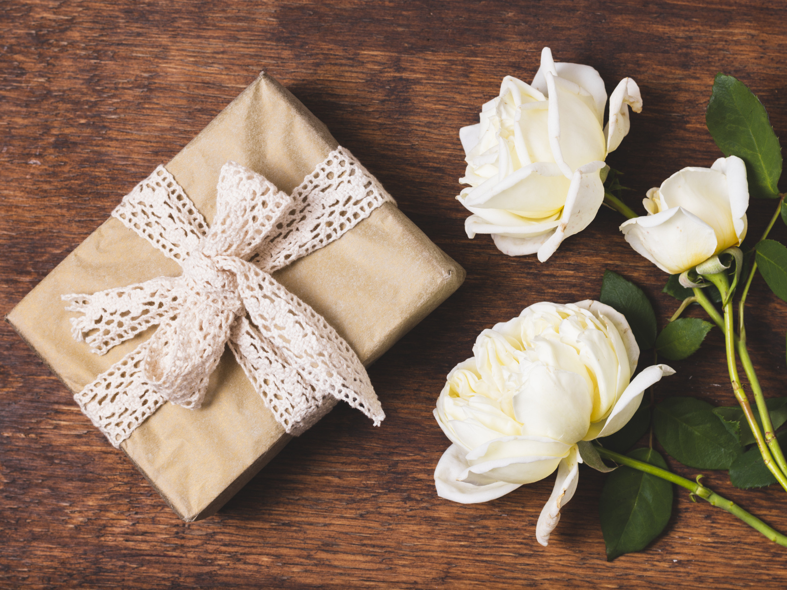 Коробка с подарком на деревянном столе с белыми розами