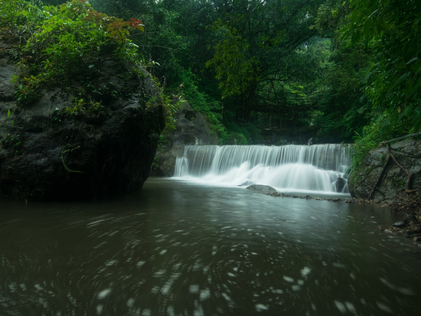 Водопад стекает в реку с большими камнями в лесу