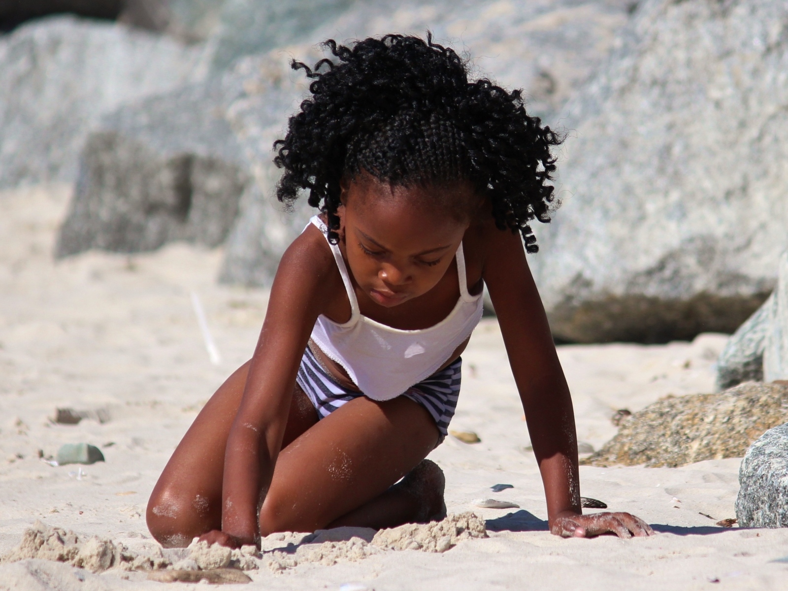 Темнокожая маленькая девочка играет на песке на пляже