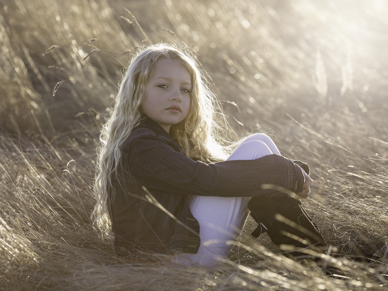 Маленькая светловолосая девочка сидит на сене