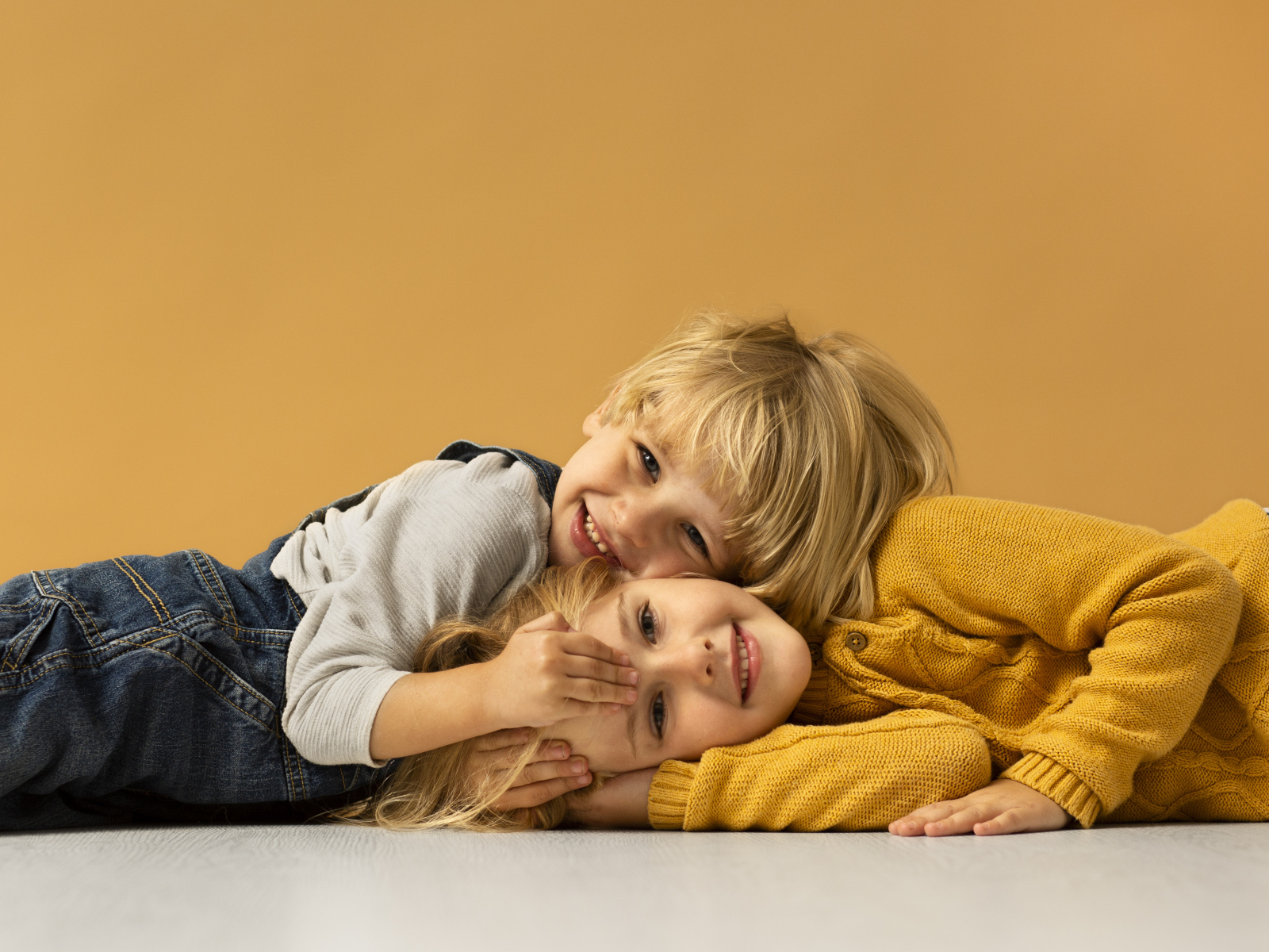 Маленькие брат и сестра лежат на полу на желтом фоне