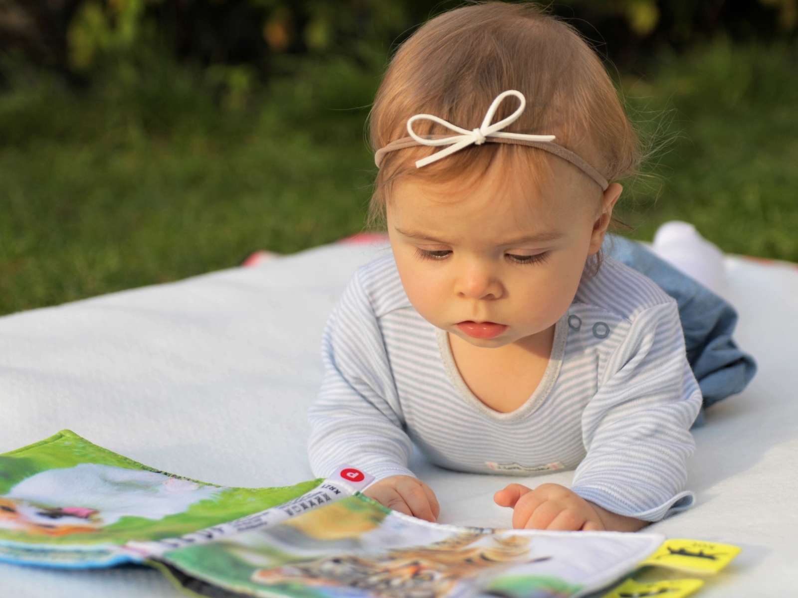 Маленькая девочка с книгой на белом покрывале