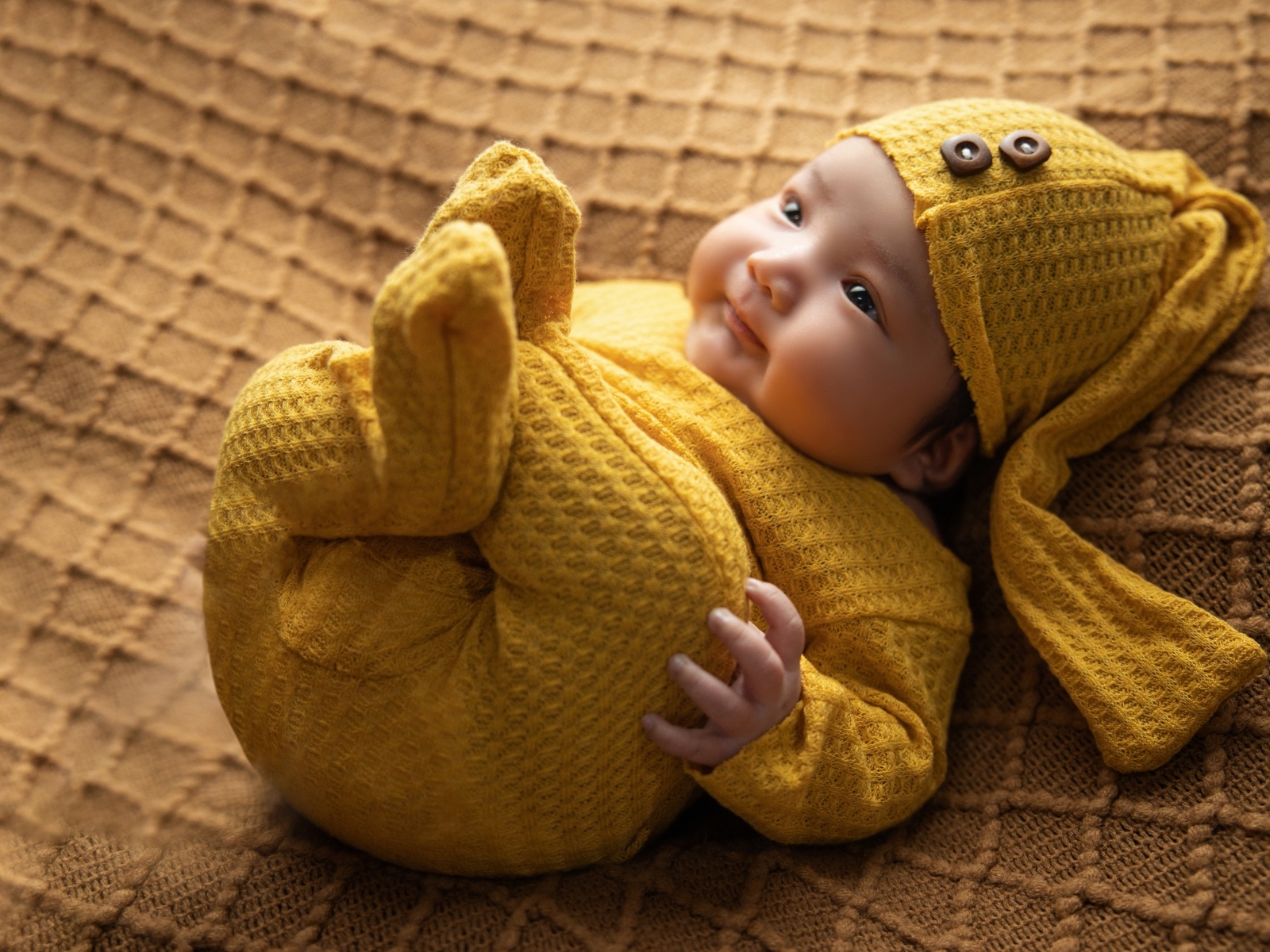Новорожденный ребенок в желтом вязаном костюме и шапке