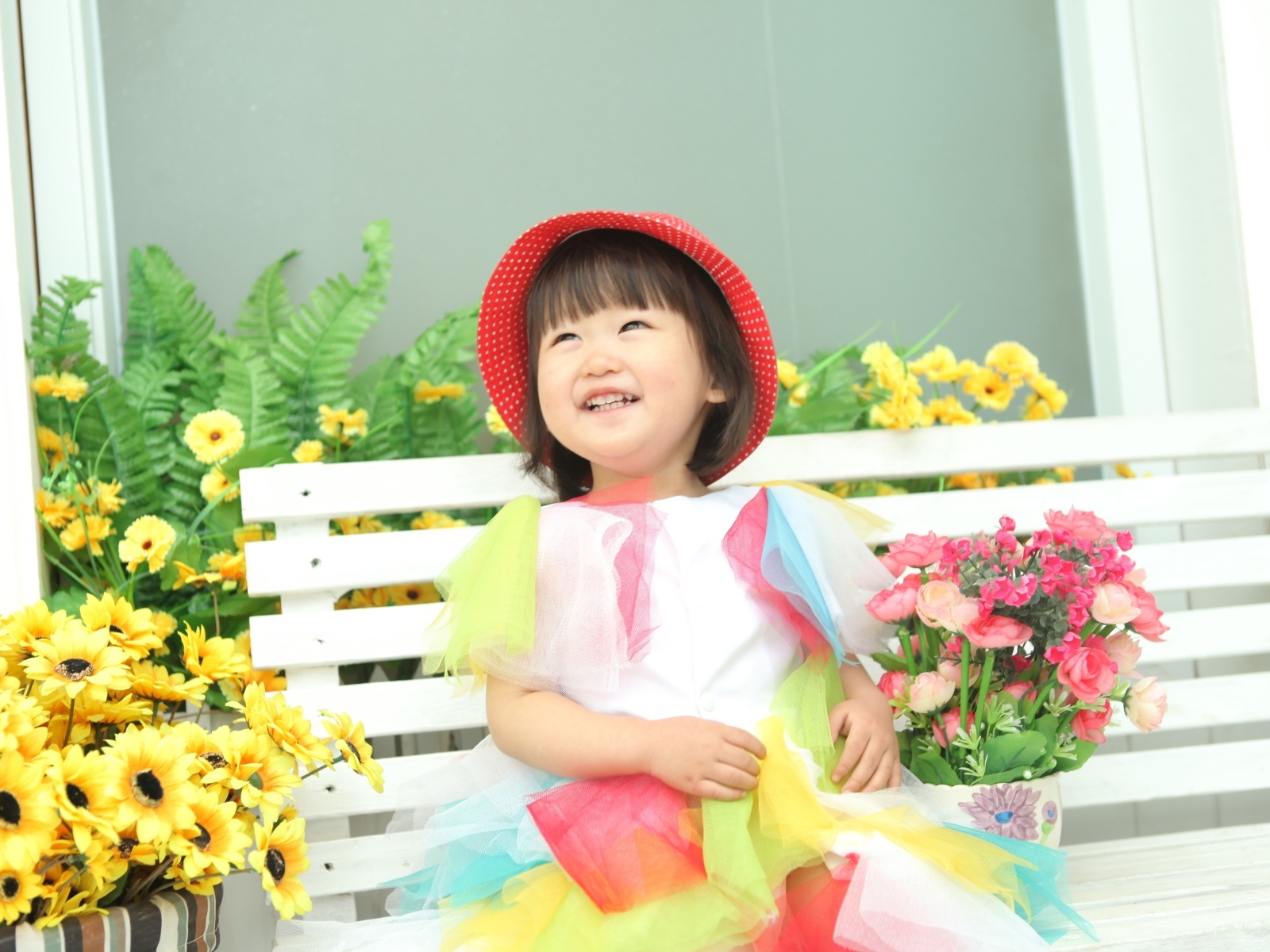 Улыбающаяся девочка азиатка сидит на лавке с цветами