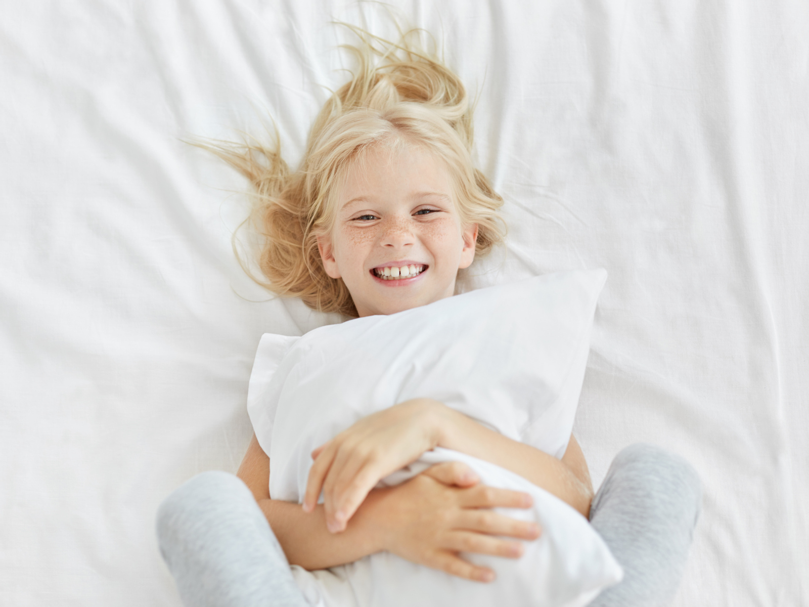Улыбающаяся маленькая девочка с подушкой на кровати